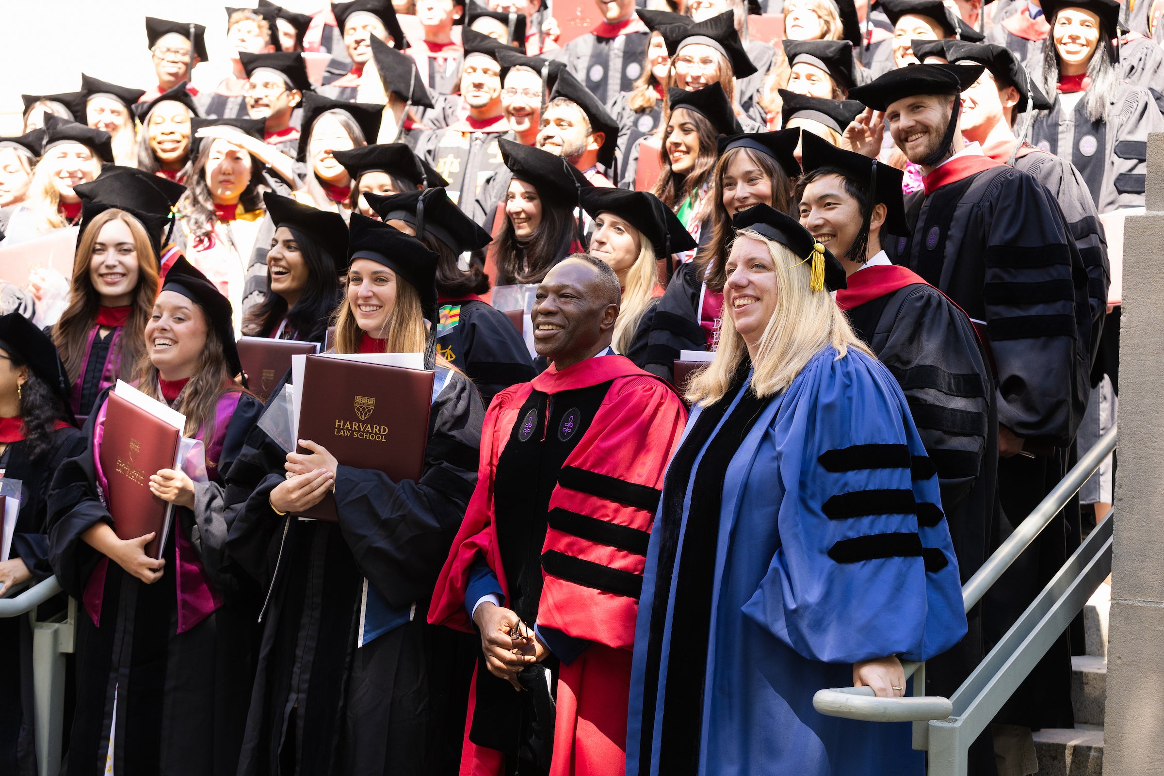 Two Harvard Law professors smile for a outdoor group photo with graduates on building steps.