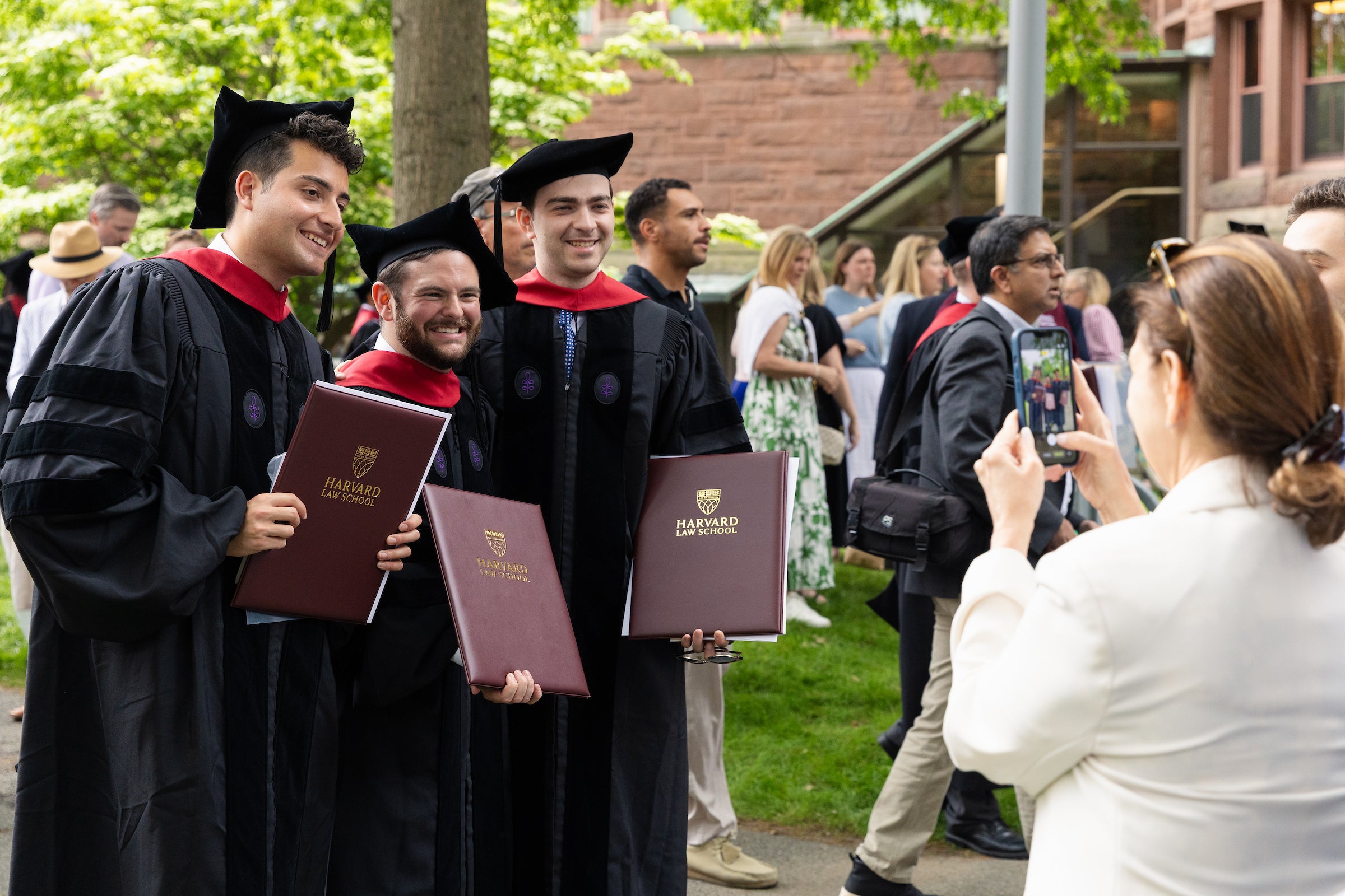 Three graduates in academic regalia smile for a photo.