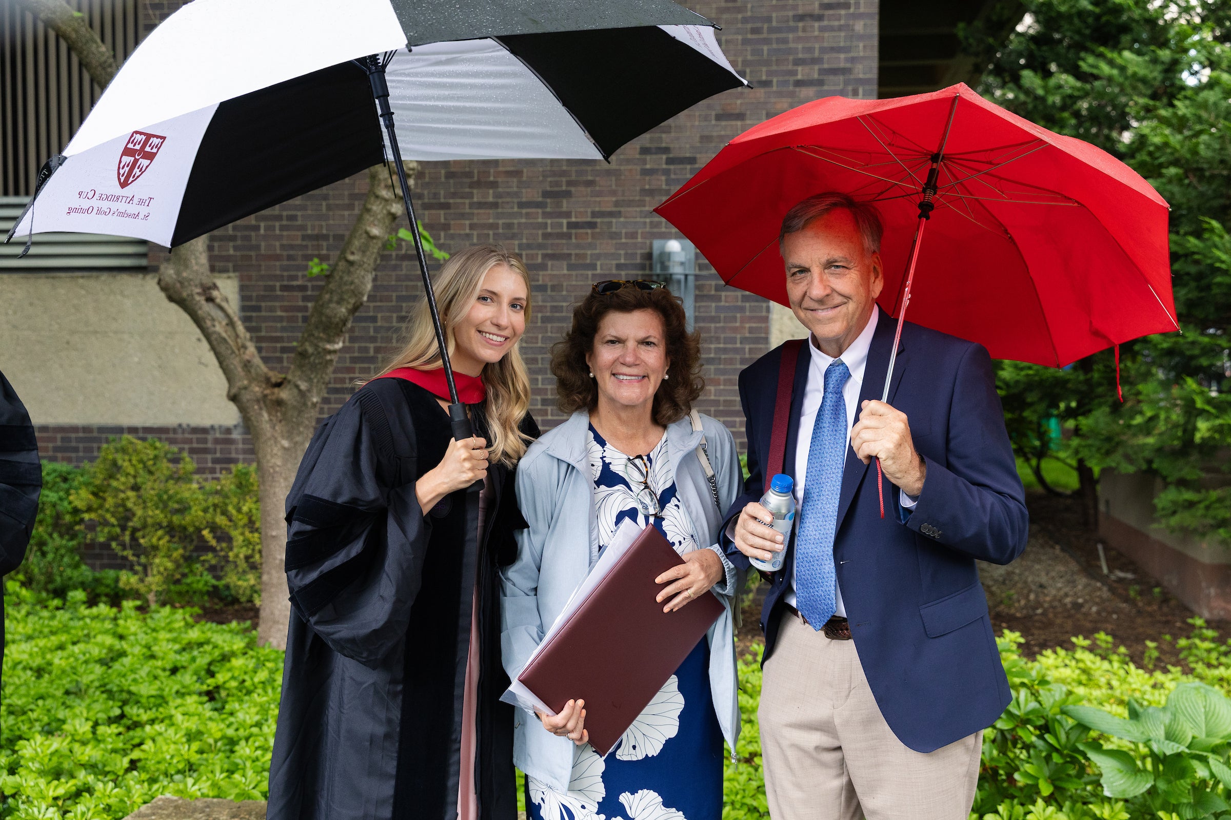 A graduate holding an umbrella smiles for a photo with her family.