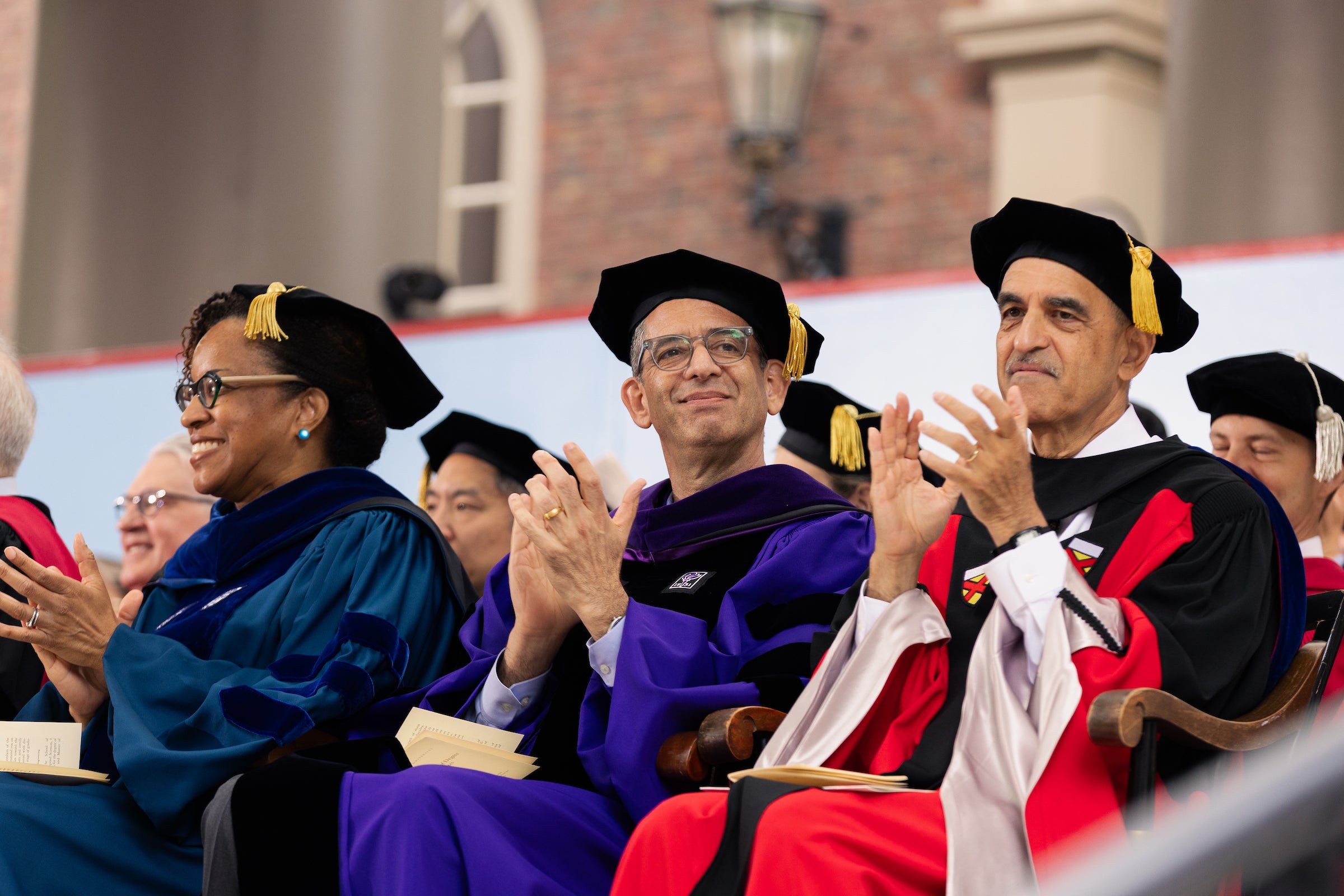 Dean Goldberg smiles and applauds while seated onstage during commencement.