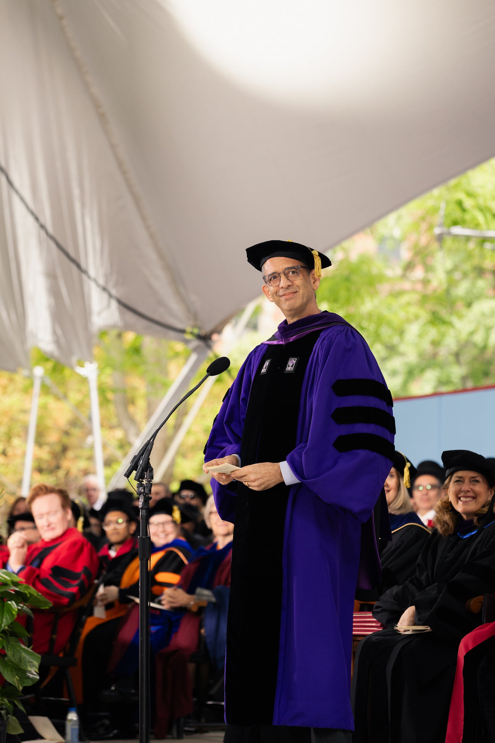 Dean Goldberg stands onstage in front of a microphone in purple regalia.