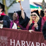 Graduates in regalia cheer and celebrate while holding a Harvard Law School banner and waving gavels.