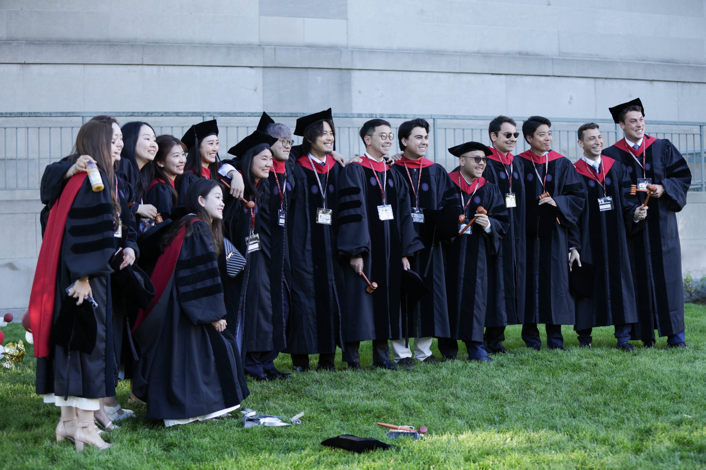 A large group of graduates, many holding gavels, pose for a photo on a grassy area.