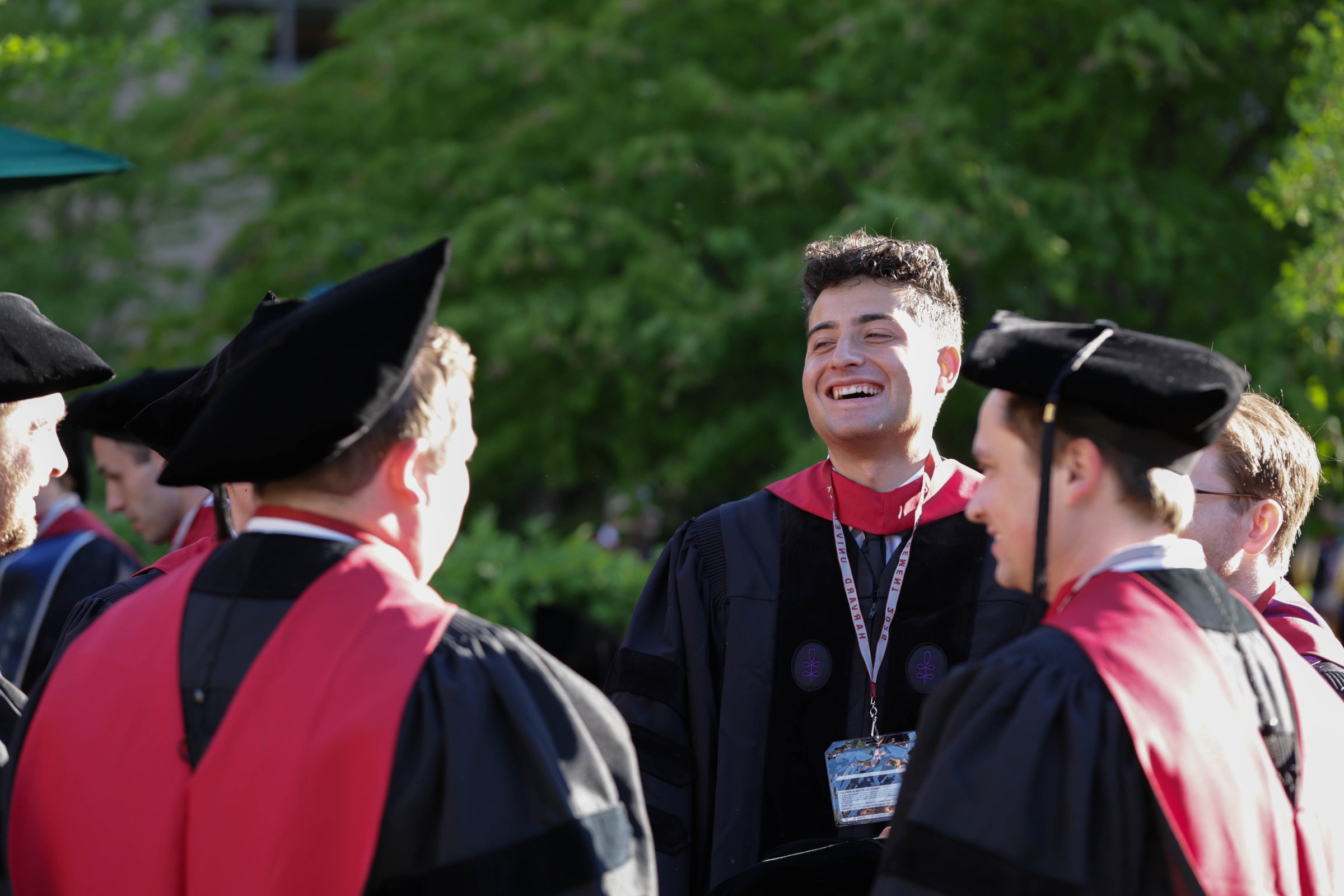 Graduates in regalia laugh and socialize outdoors.