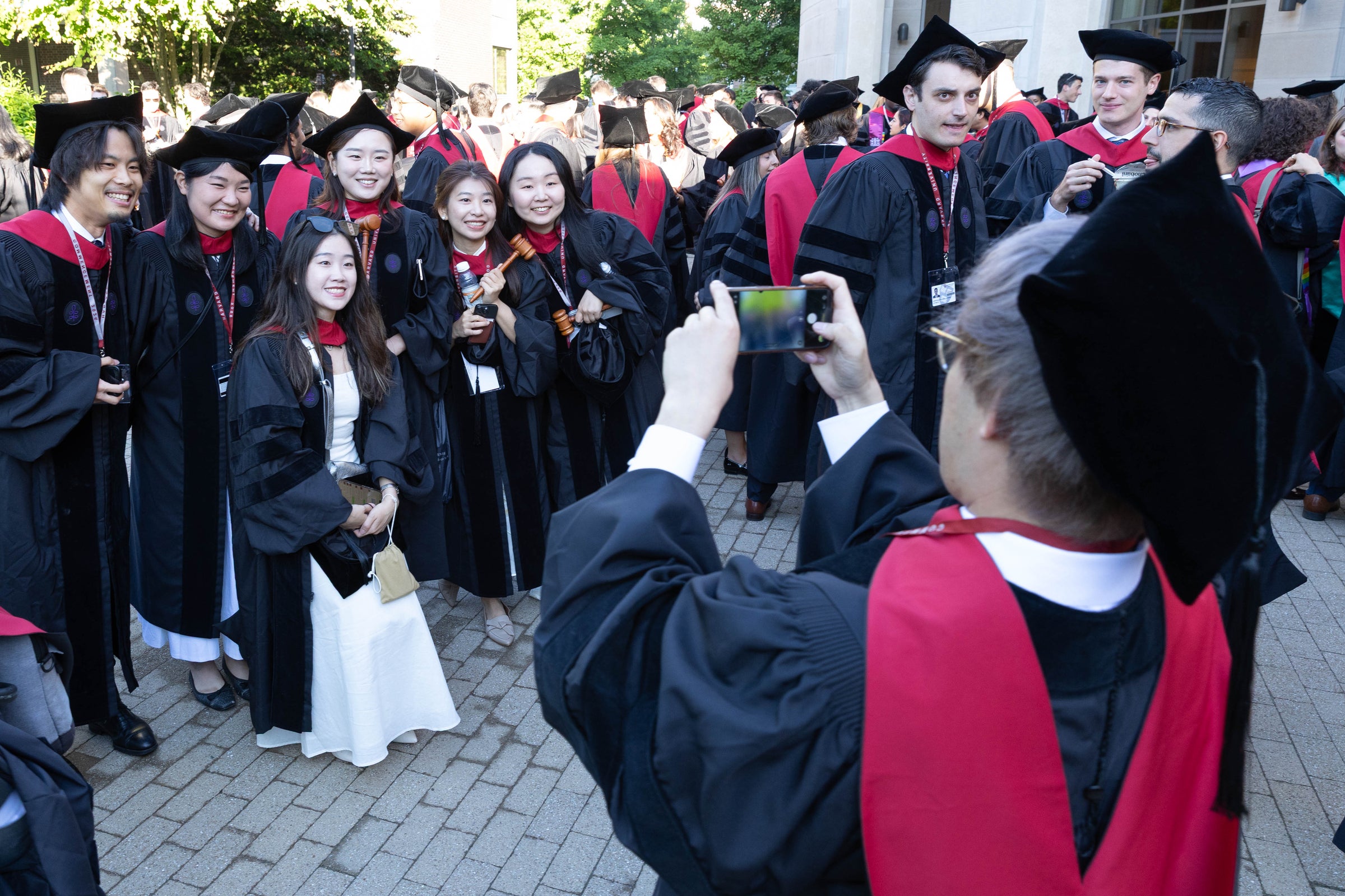 Graduates in black and red regalia pose for photos outdoors.