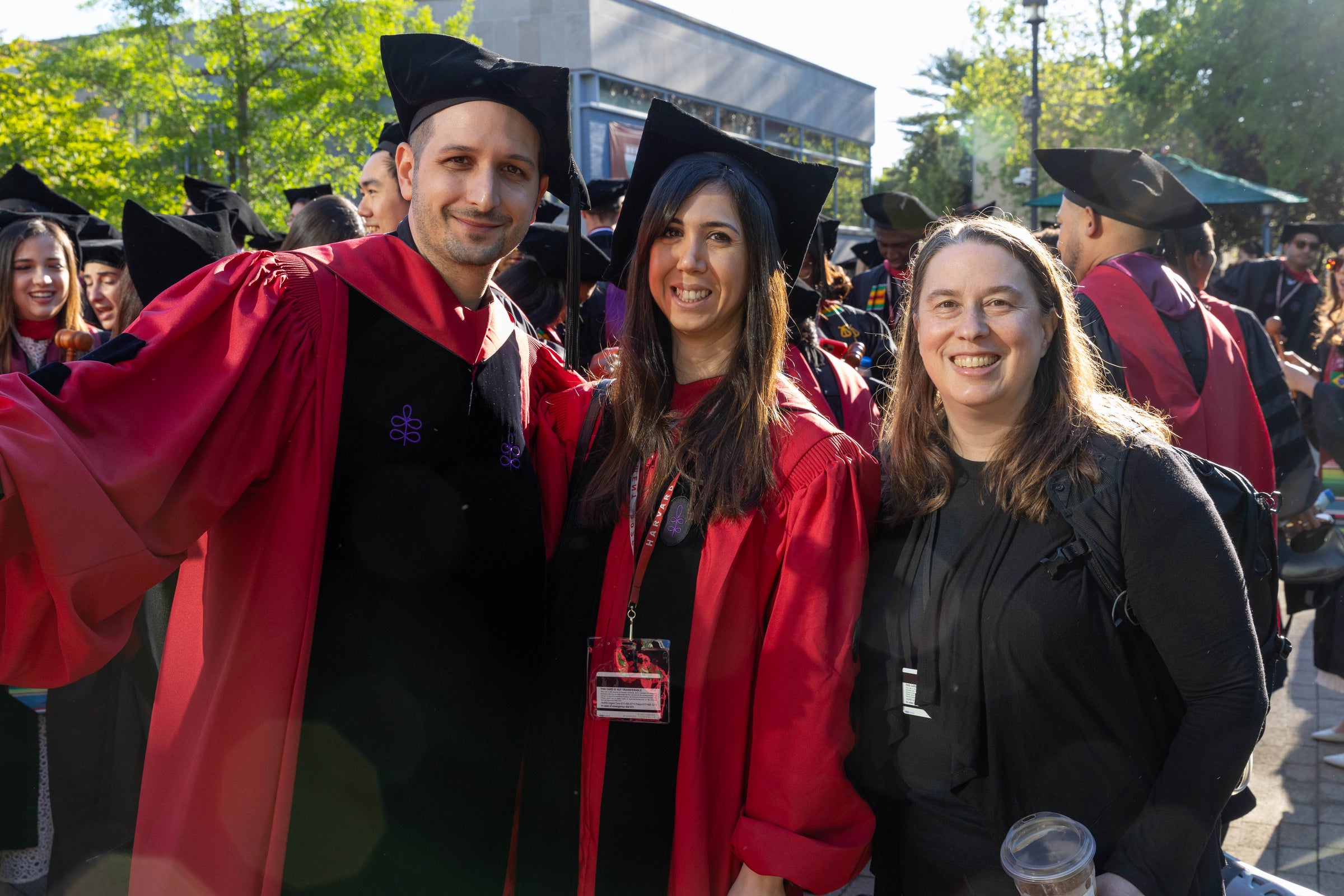 Three individuals - two graduates in regalia - smile for the camera at an outdoor event.
