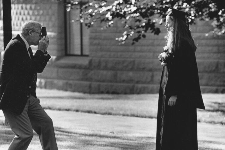 A black and white historical photograph of a man taking a picture of a graduating student.