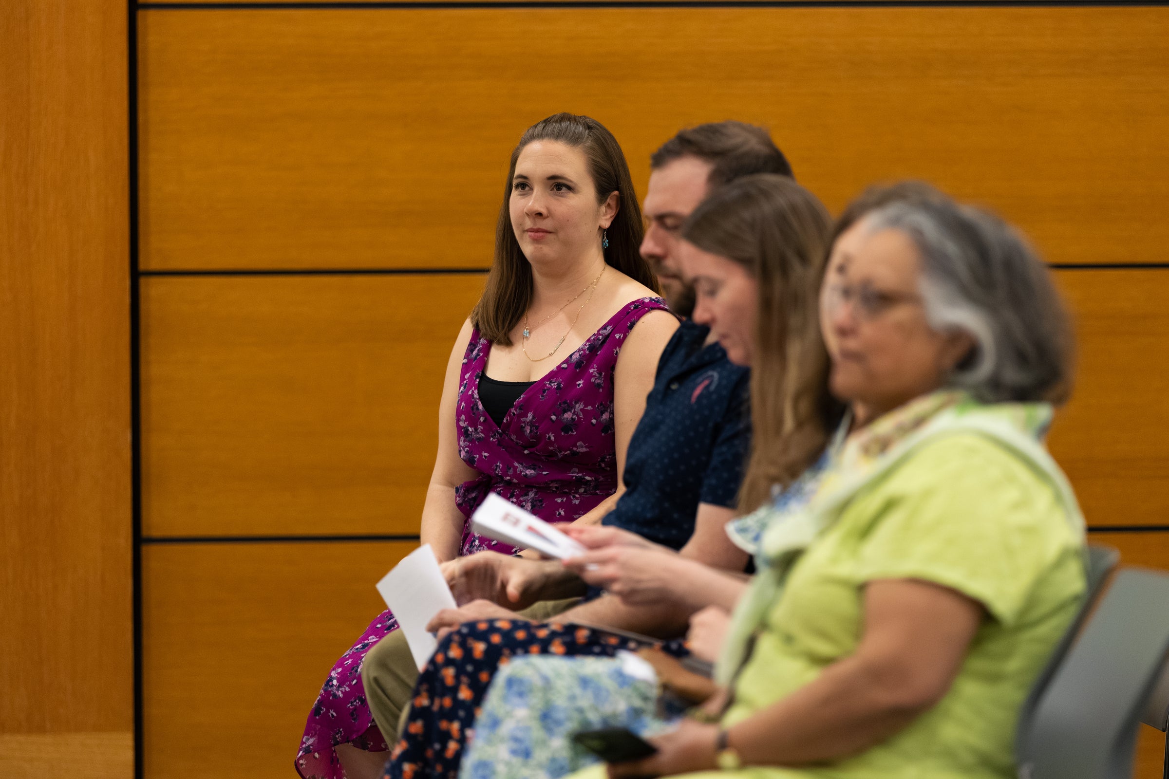A group of people seated in a row listen attentively to a speaker.