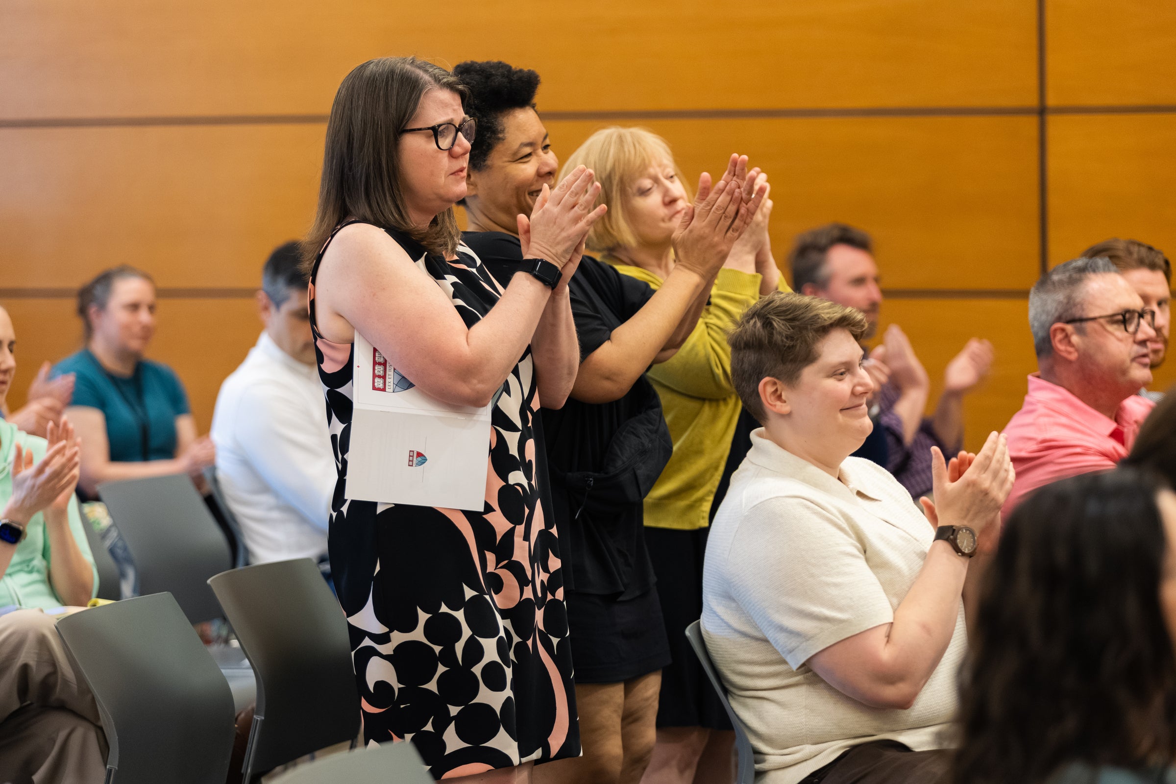 Three people stand up in an audience and clap their hands in applause.