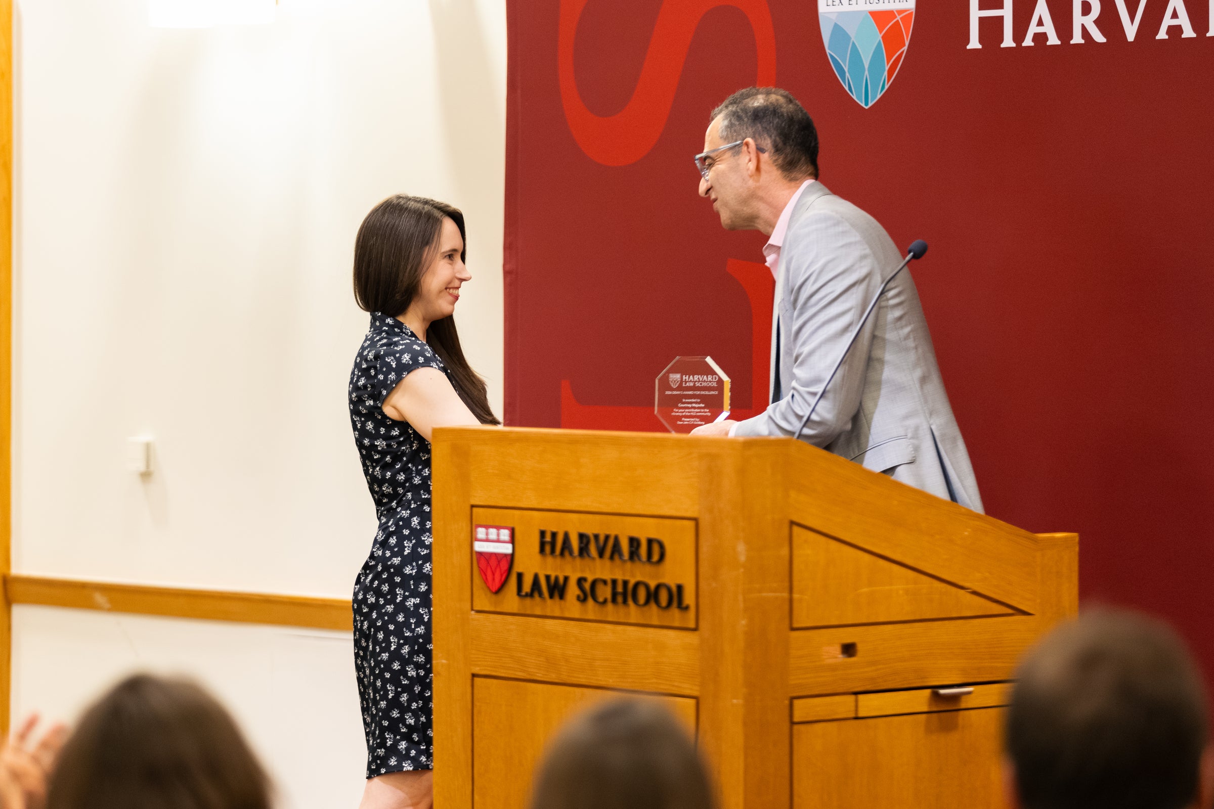 A person in a patterned dress accepts an award from Dean Goldberg next to a podium.