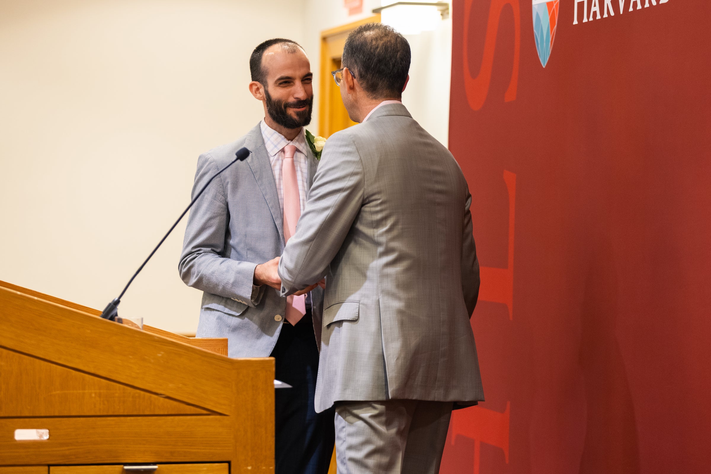 A person in a gray suit accepts an award from Dean Goldberg next to a podium.