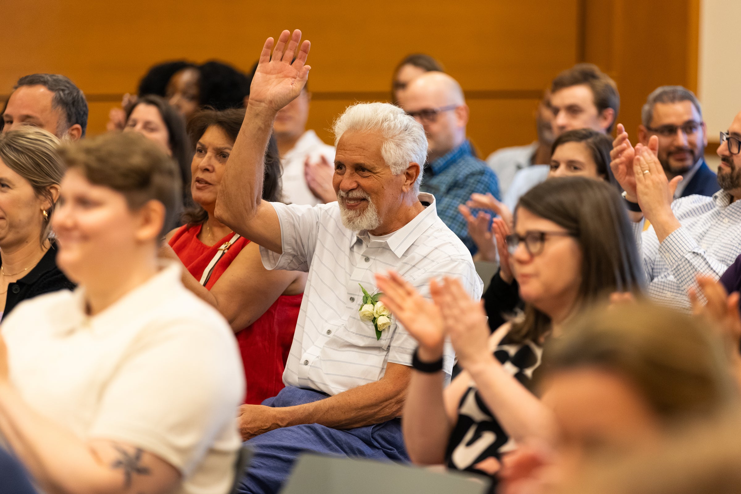 An individual raises his hand in a seated audience while others around him clap.