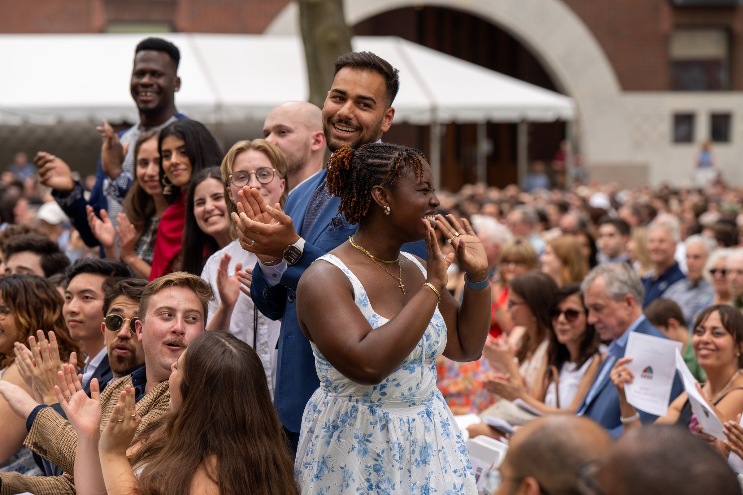 A person in a blue and white floral dress waves to an audience as she receives a round of applause.