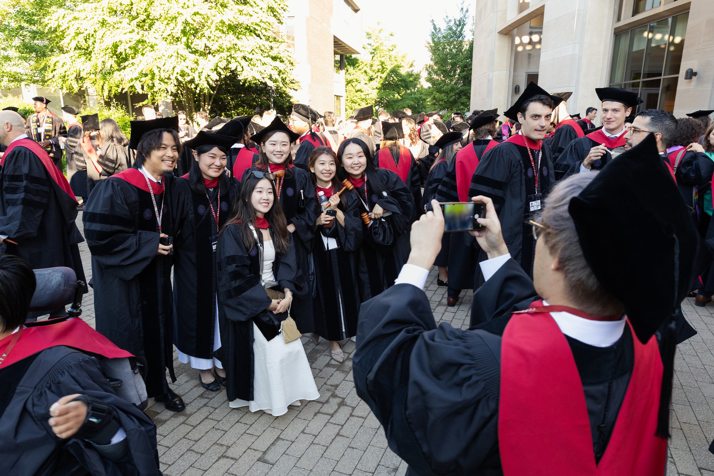 Graduates in black and red regalia pose for photos outdoors.