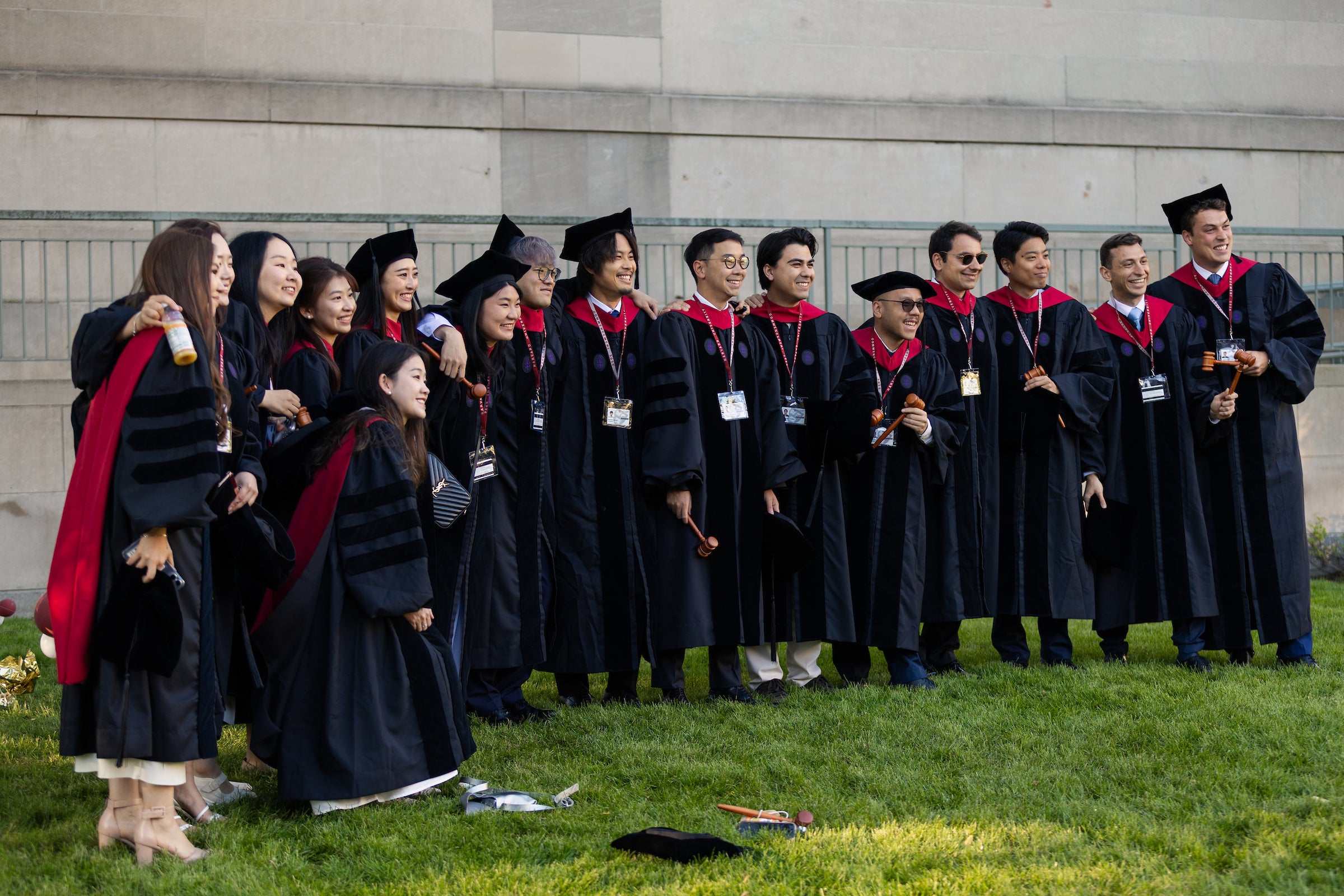 A large group of graduates, many holding gavels, pose for a photo on a grassy area.