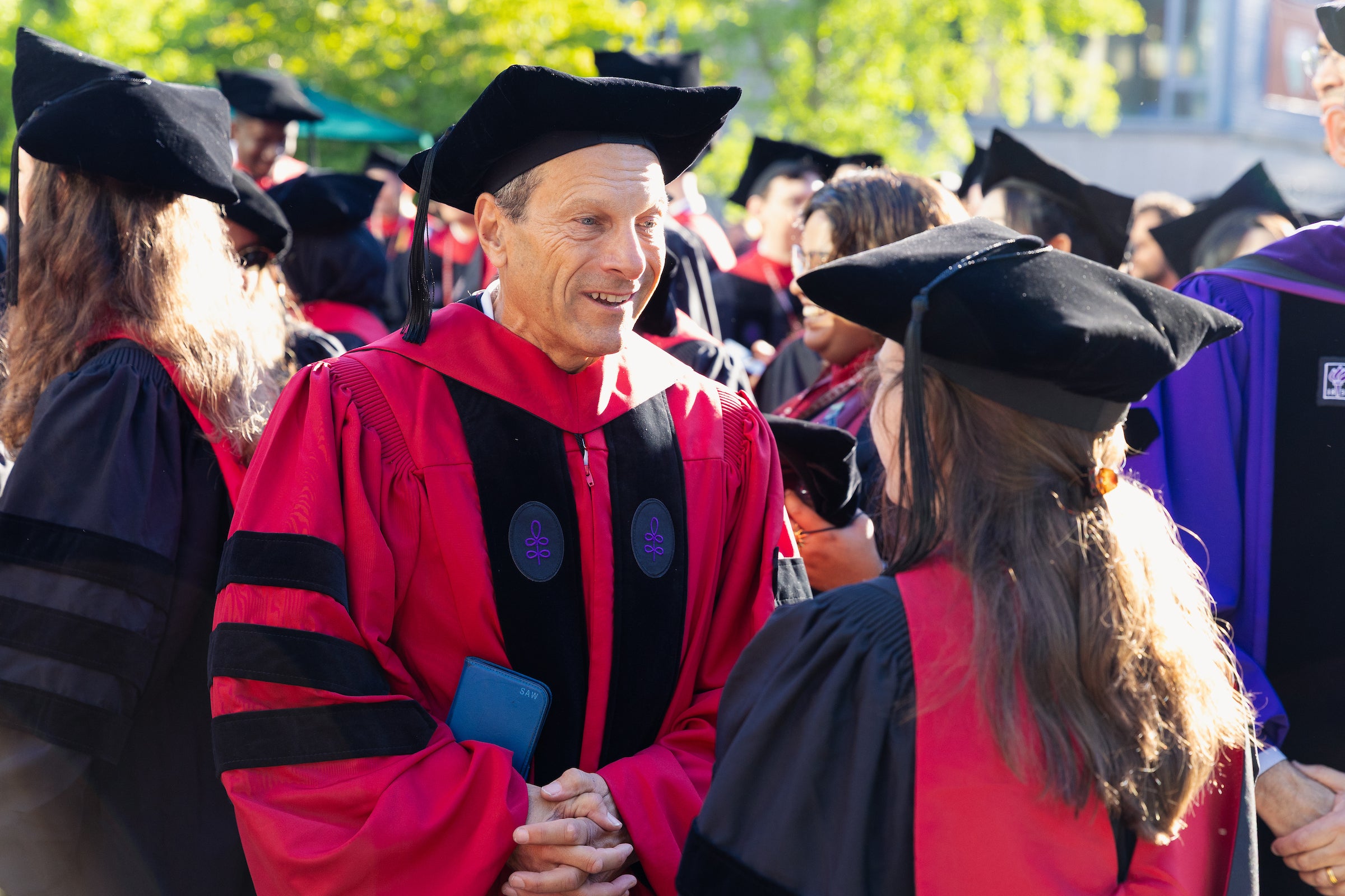A faculty member in academic regalia speaks with a graduate at an outdoor event.