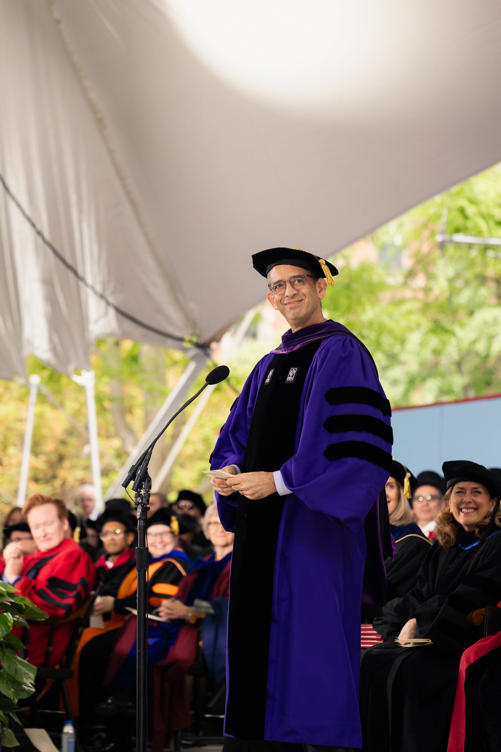 Dean Goldberg stands onstage in front of a microphone in purple regalia.