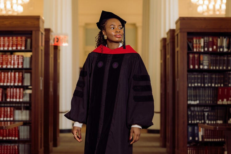A student in graduation attire poses inside Langdell Hall reading room.
