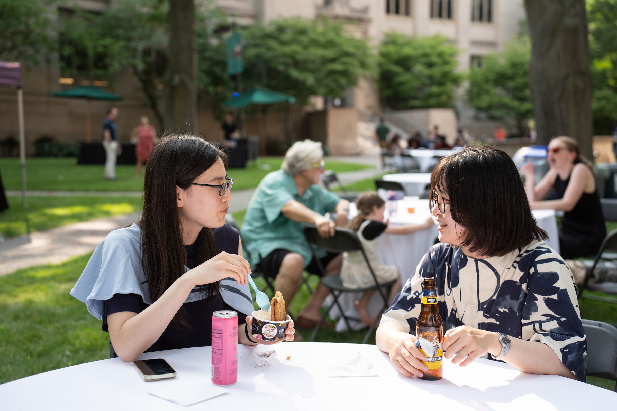Two individuals enjoy food and drink together at a circular table under a sunny sky.