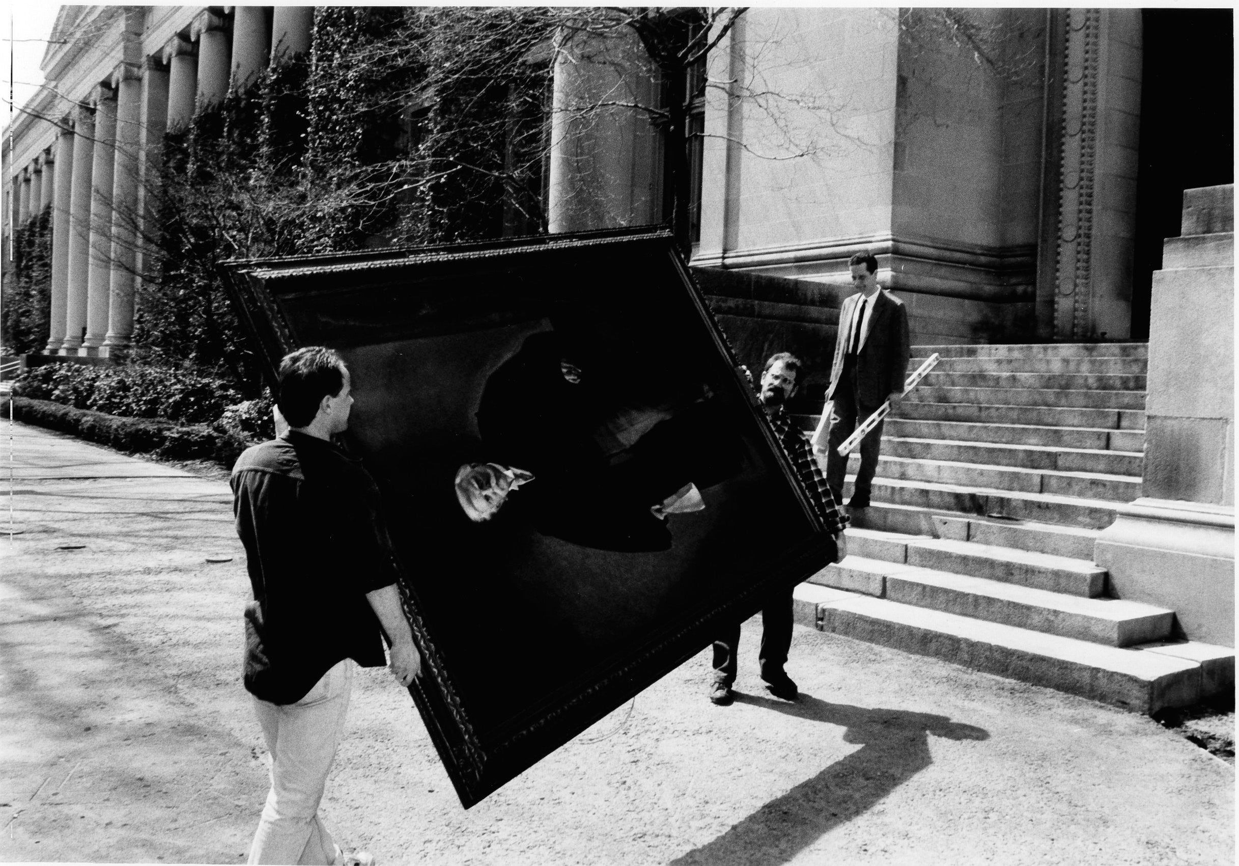 Two men carrying a large framed painting on campus.