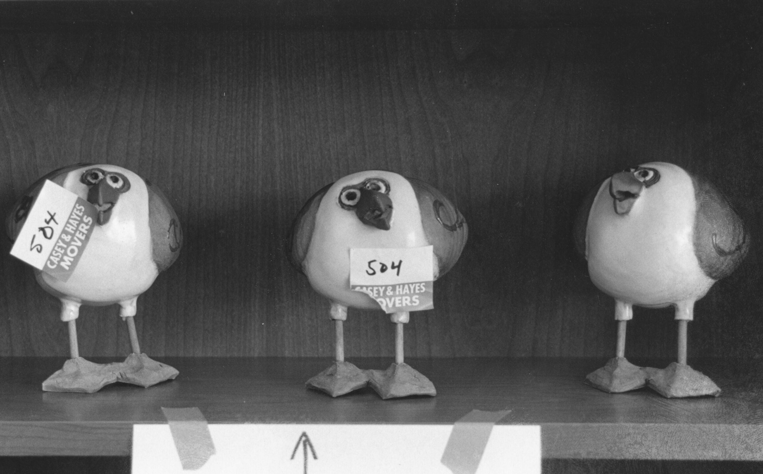 Three clay ducks on a bookshelf with moving tags.