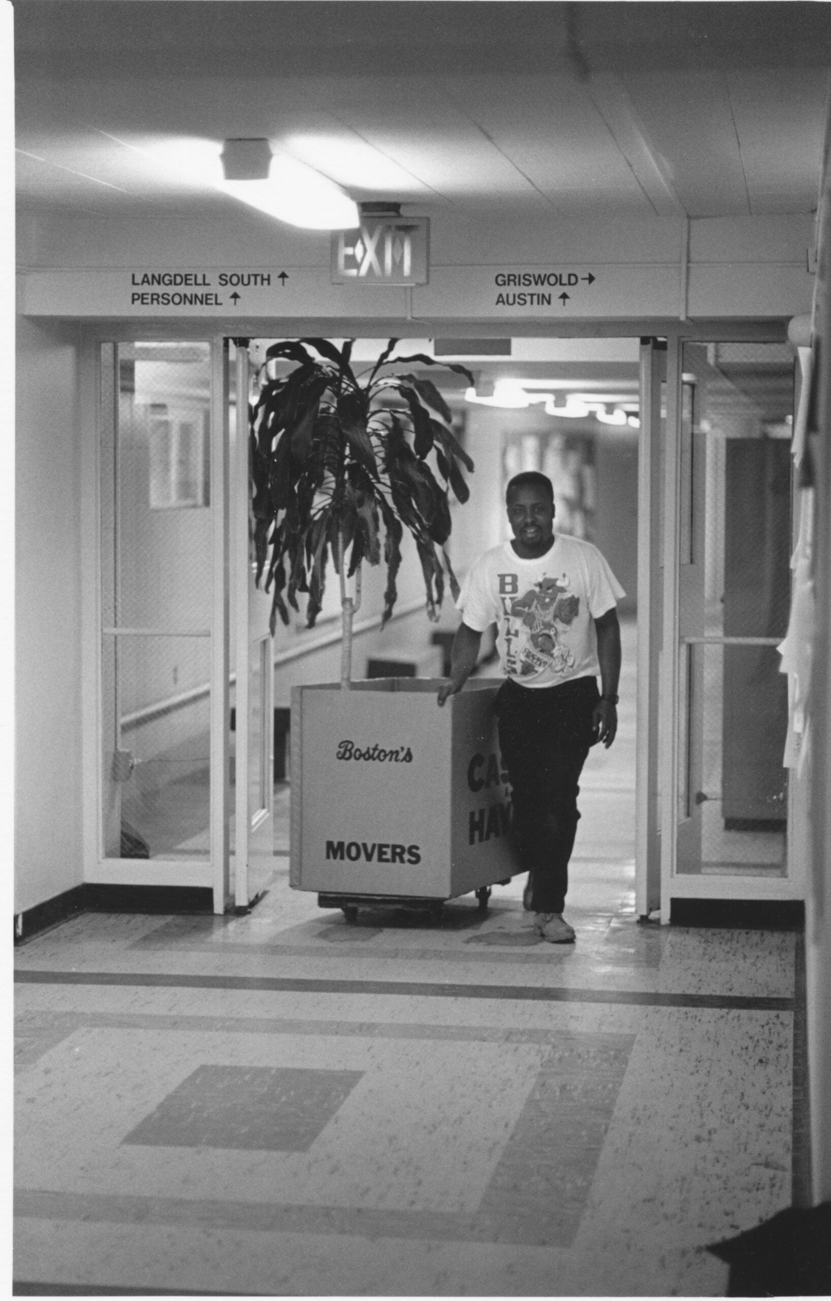 A mover pulls a box of items, and a large plant through the building tunnels to a new building.