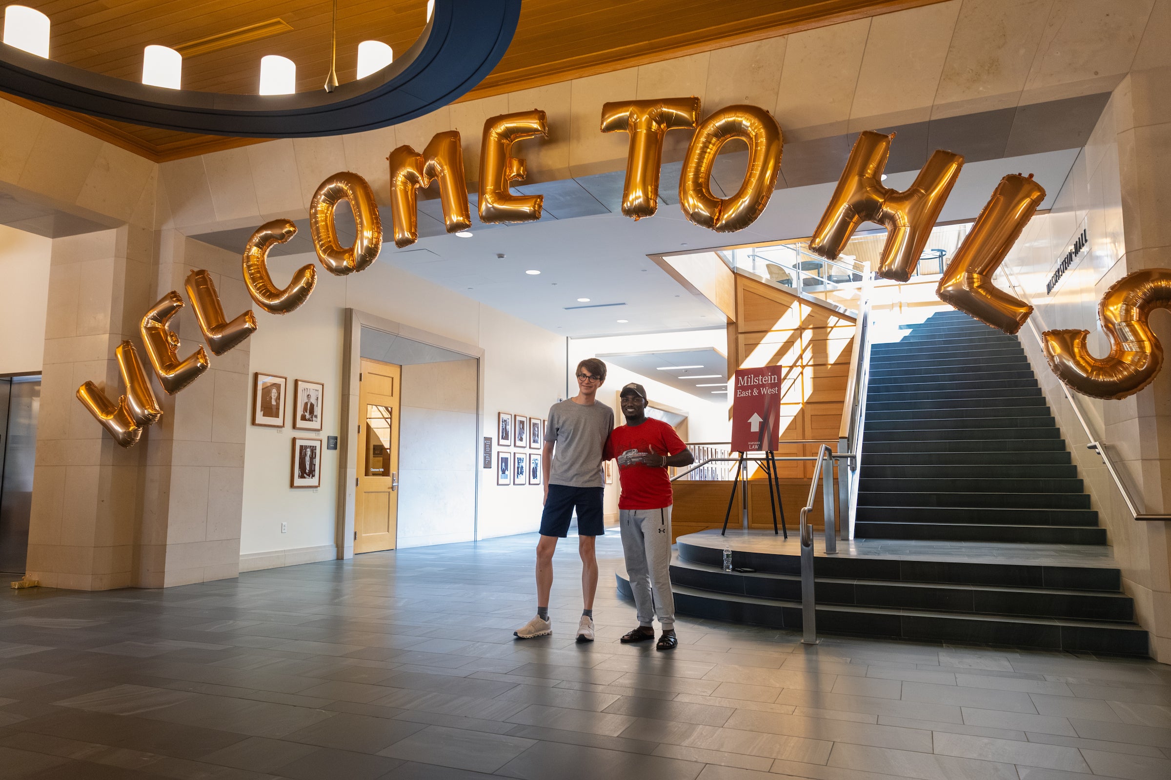 Two students stand beneath large gold balloons spelling 