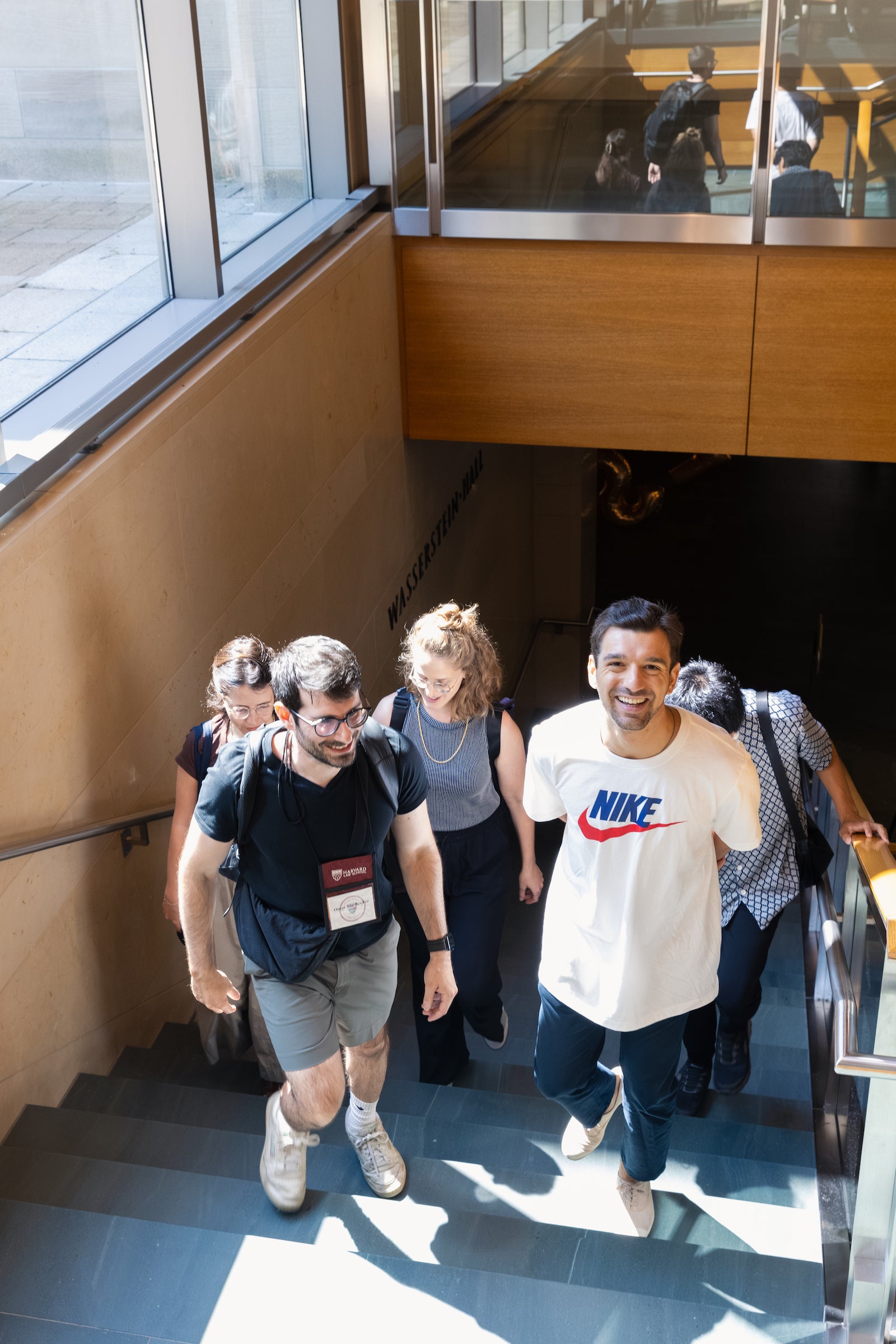 A group of students walk up a modern staircase in a well-lit building, with one individual smiling directly at the camera.