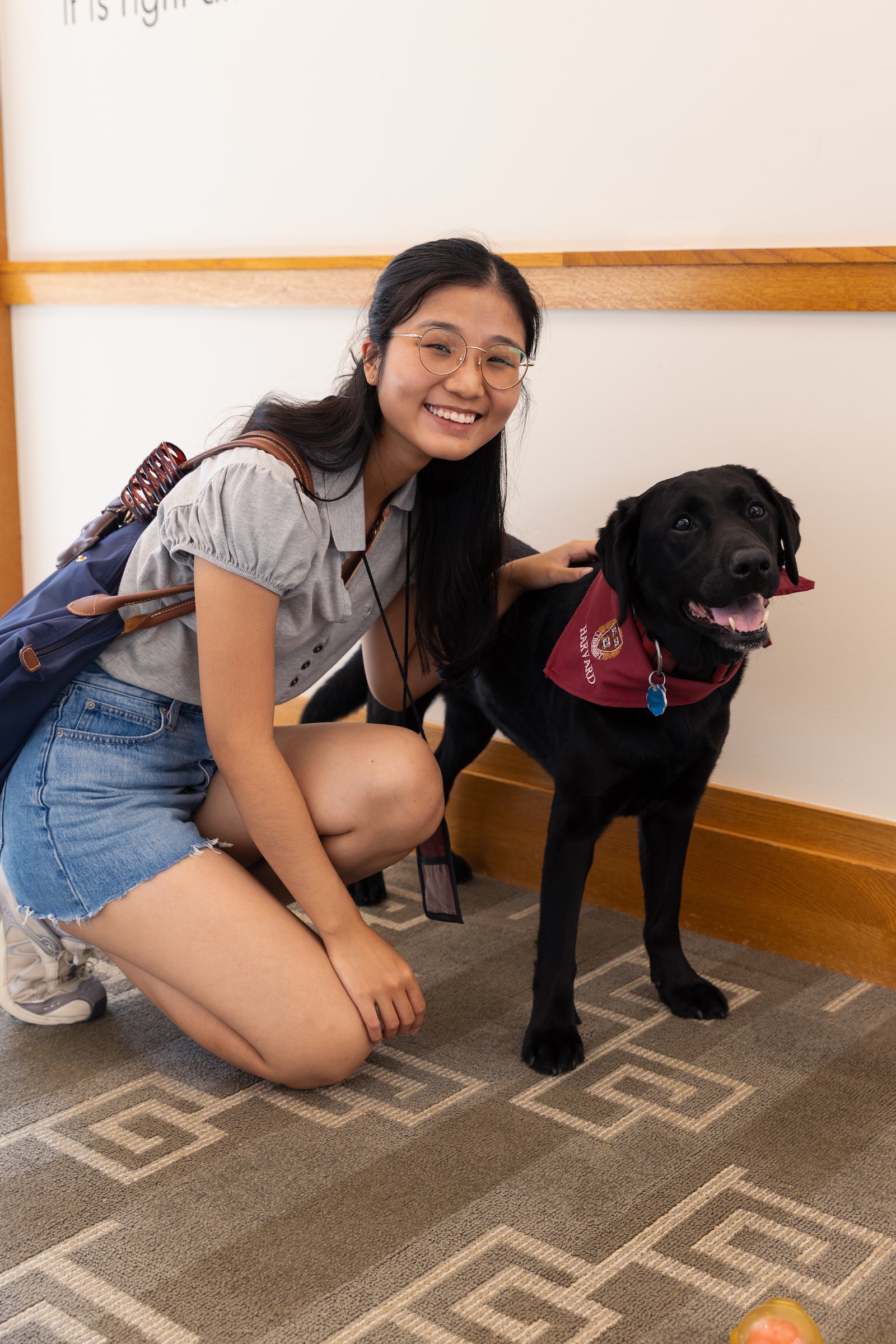 A student crouches beside a black dog wearing a red bandana, both smiling at the camera.