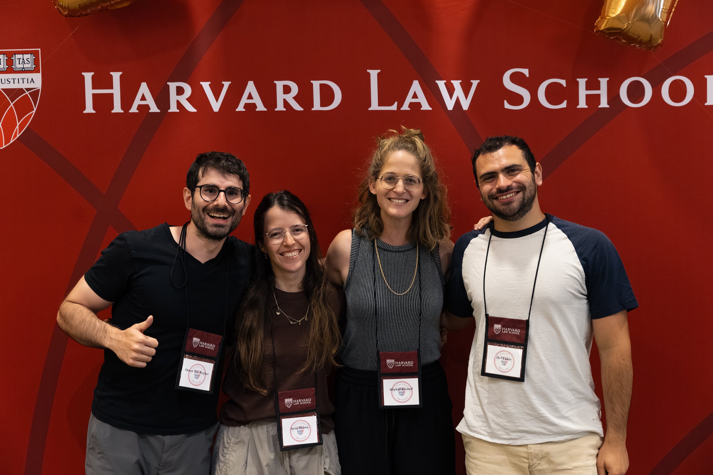 Four individuals pose together in front of a Harvard Law School backdrop.