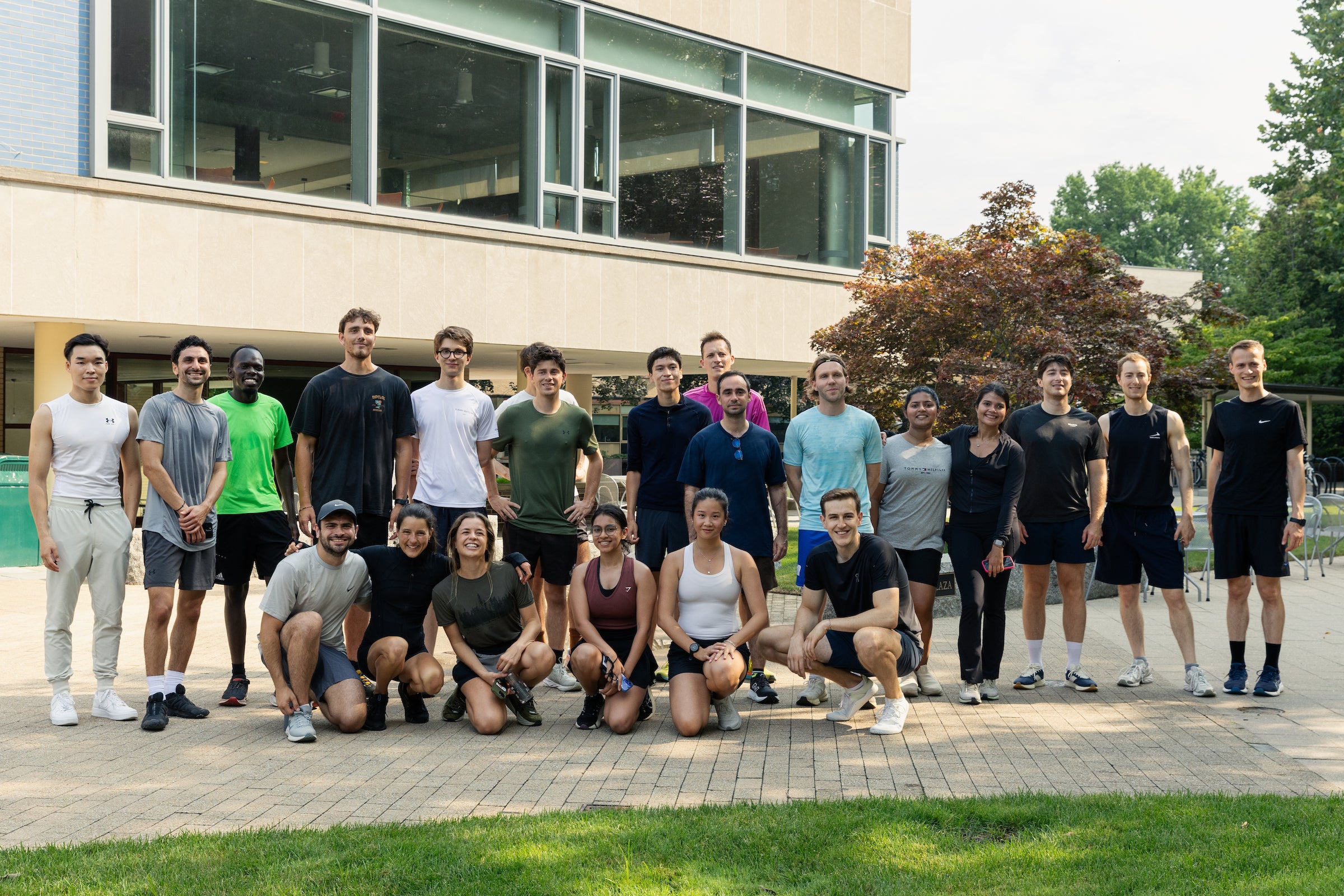 A group of students in athletic wear pose together outdoors in front of a modern building.