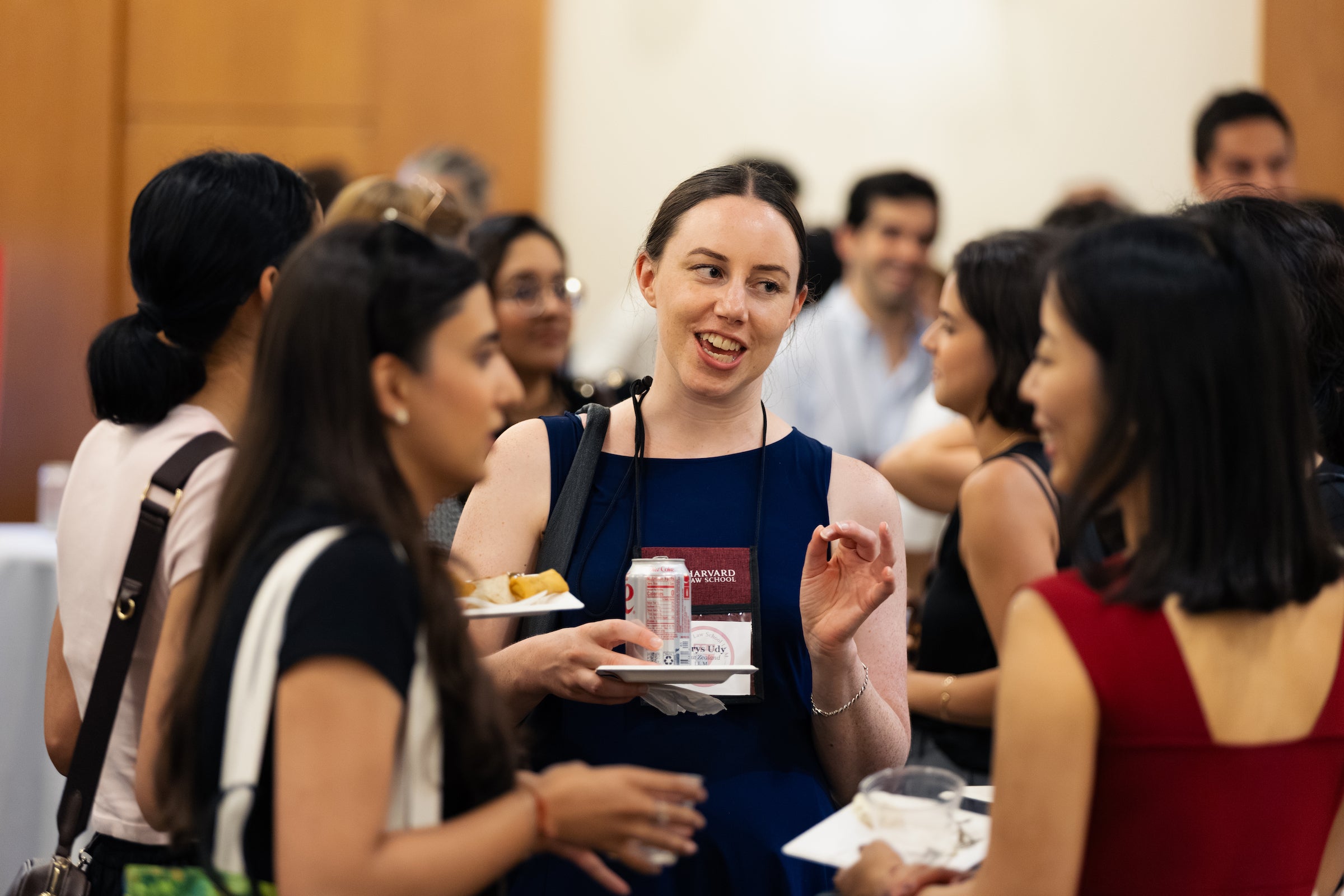 A student holds a plate of food and a can while engaging in conversation at a social gathering.