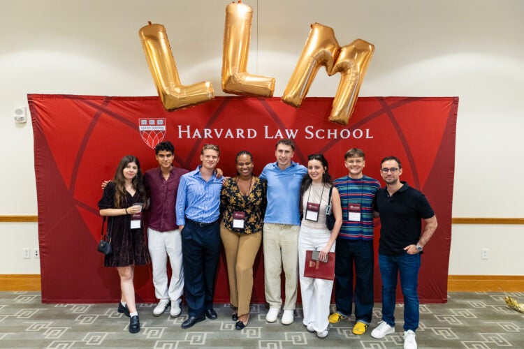 Eight new LL.M. students at Harvard Law School pose in front of a crimson backdrop and golden balloons.