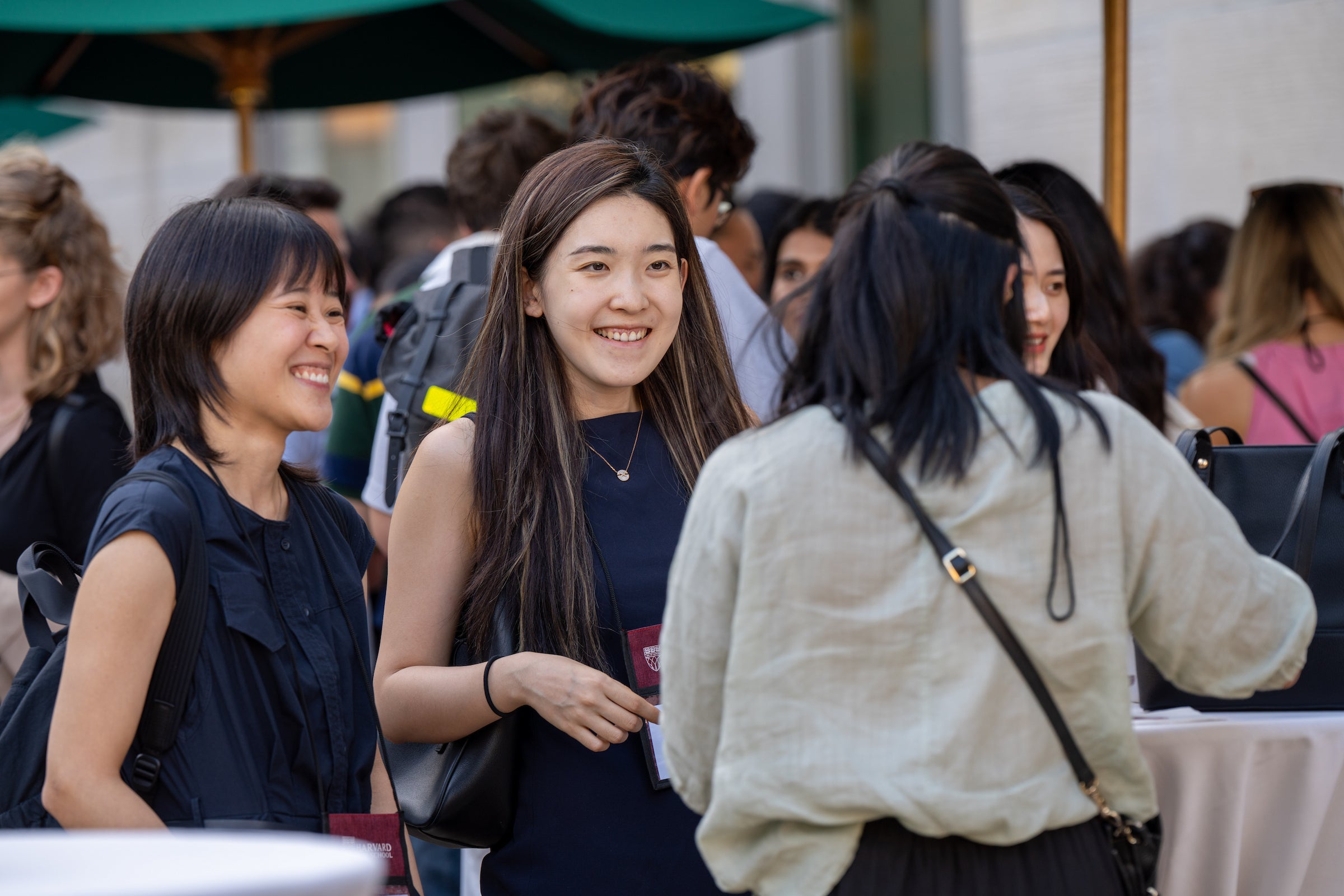 A group of students socialize outdoors under a green umbrella, smiling and engaged in conversation.