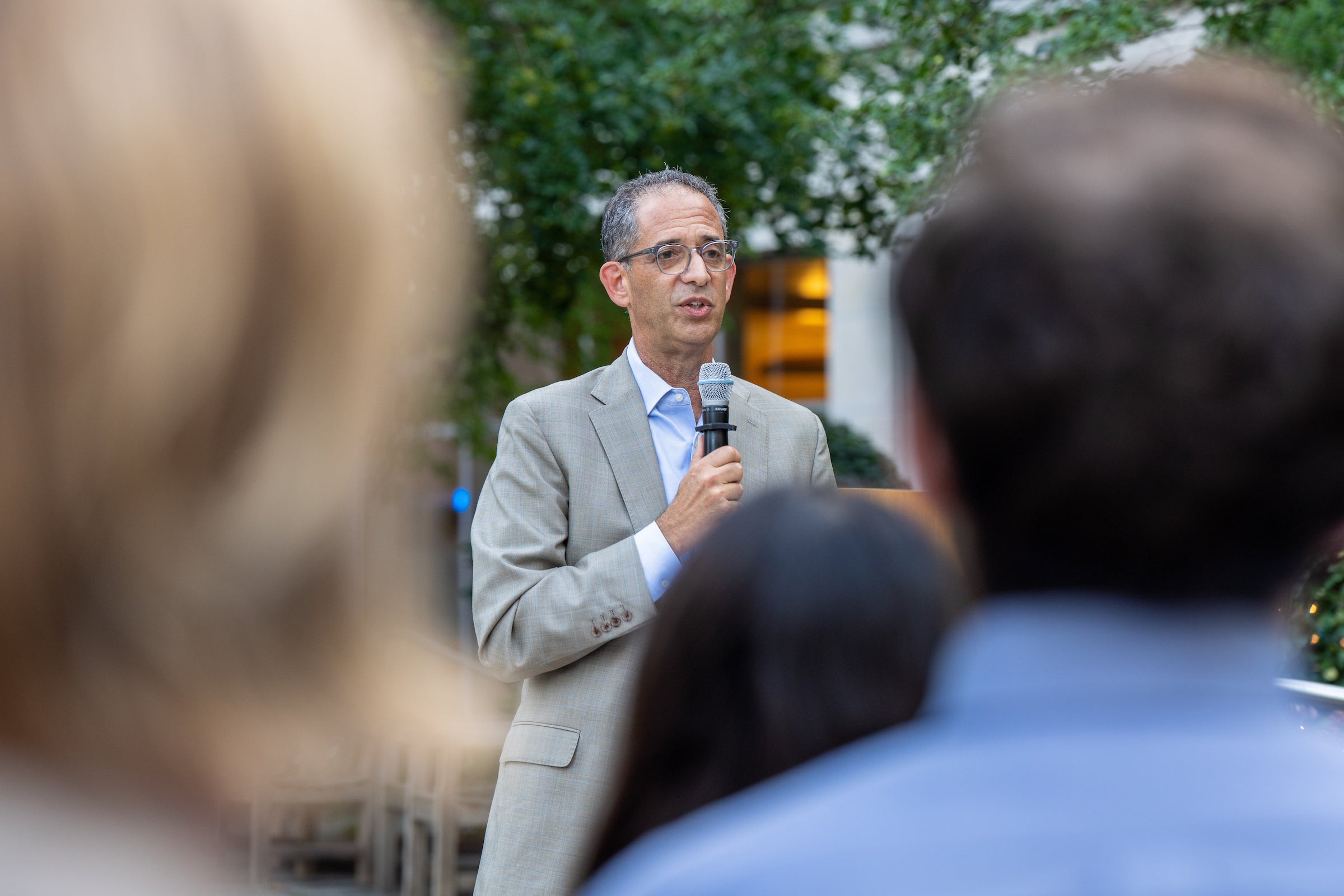 The dean speaks into a microphone while addressing students outdoors.