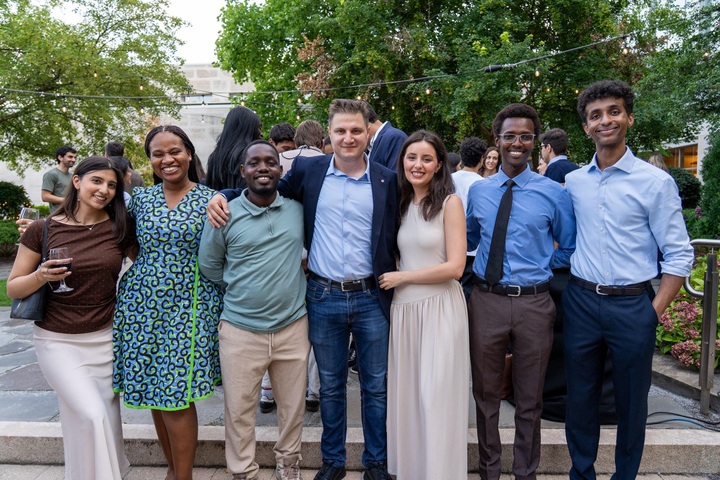 A group of seven students pose together outdoors at an event, smiling for the camera under string lights.