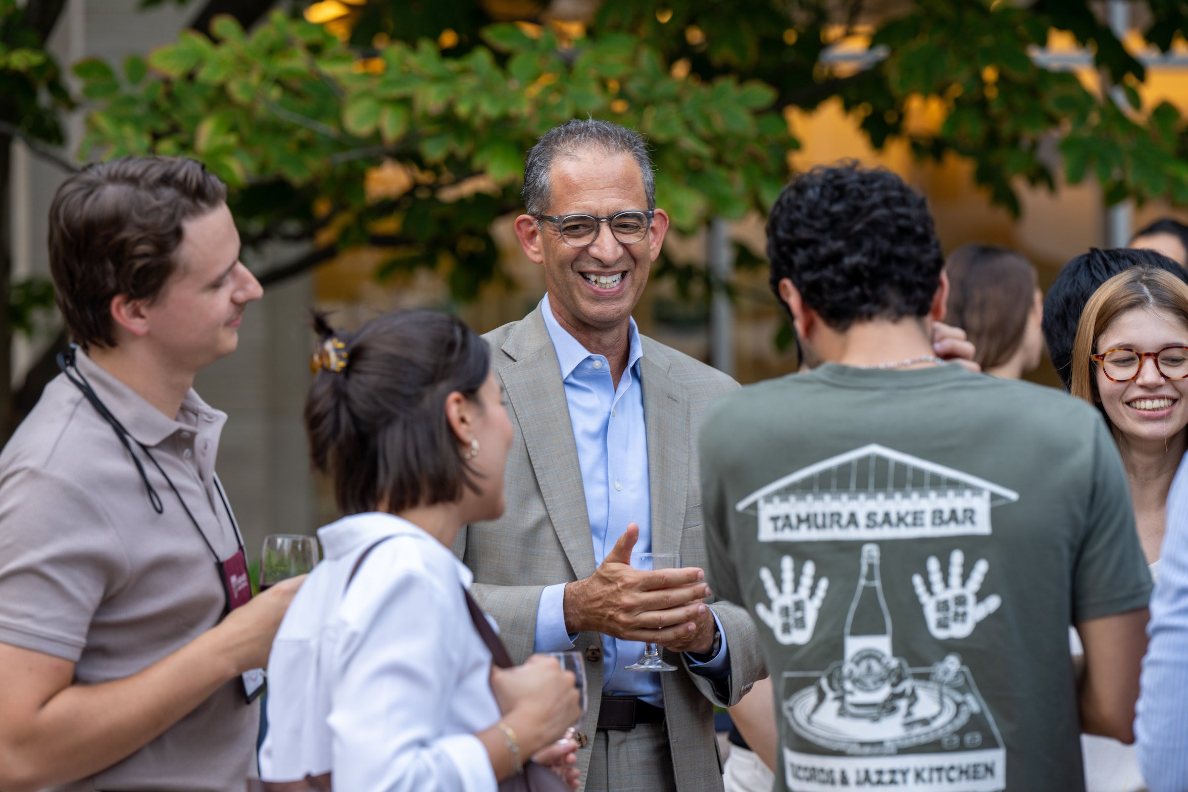 A group of students socialize and laugh with the dean outdoors.