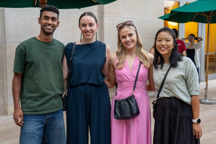 Four students pose together outdoors under green umbrellas, smiling for the camera.