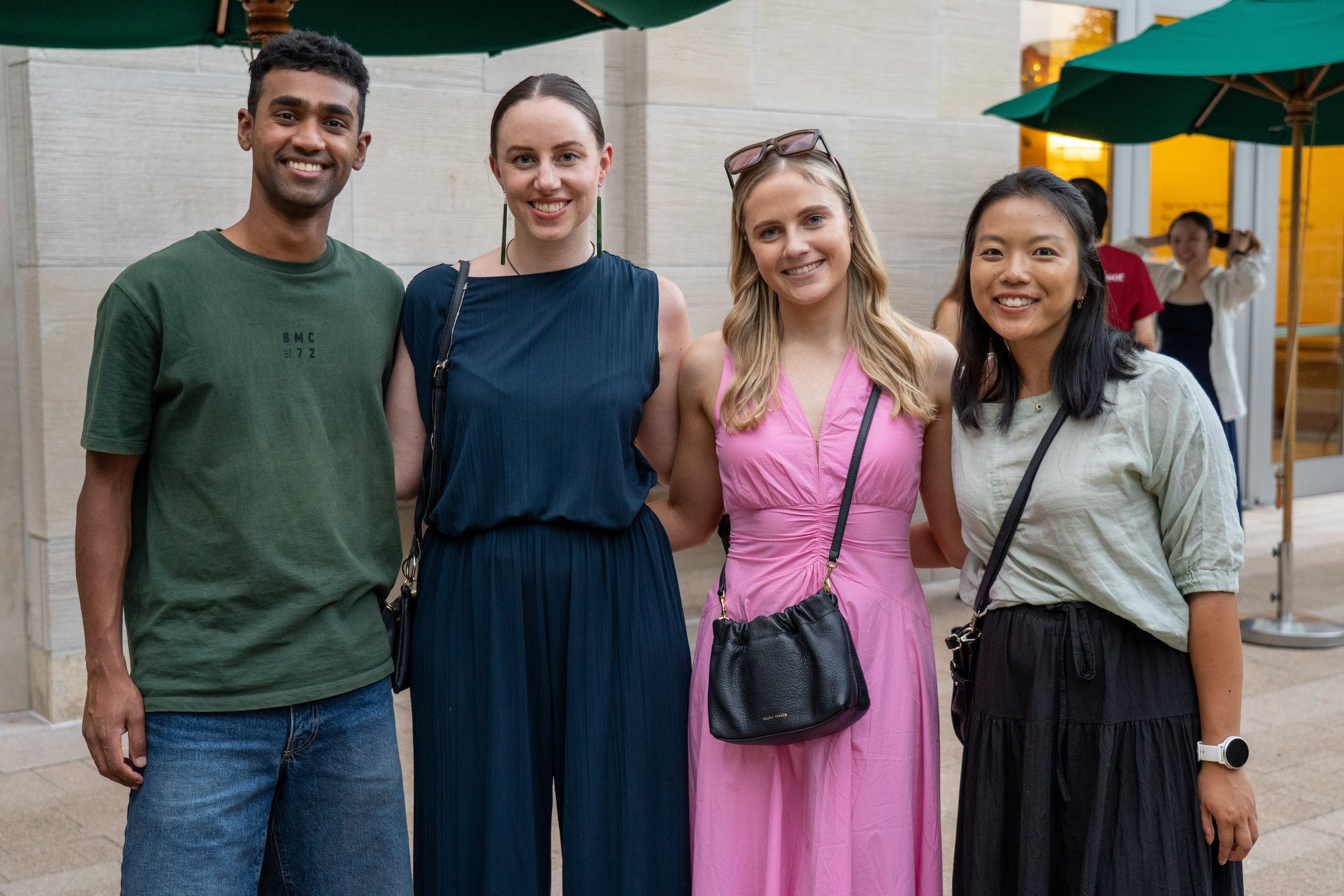 Four students pose together outdoors under green umbrellas, smiling for the camera.