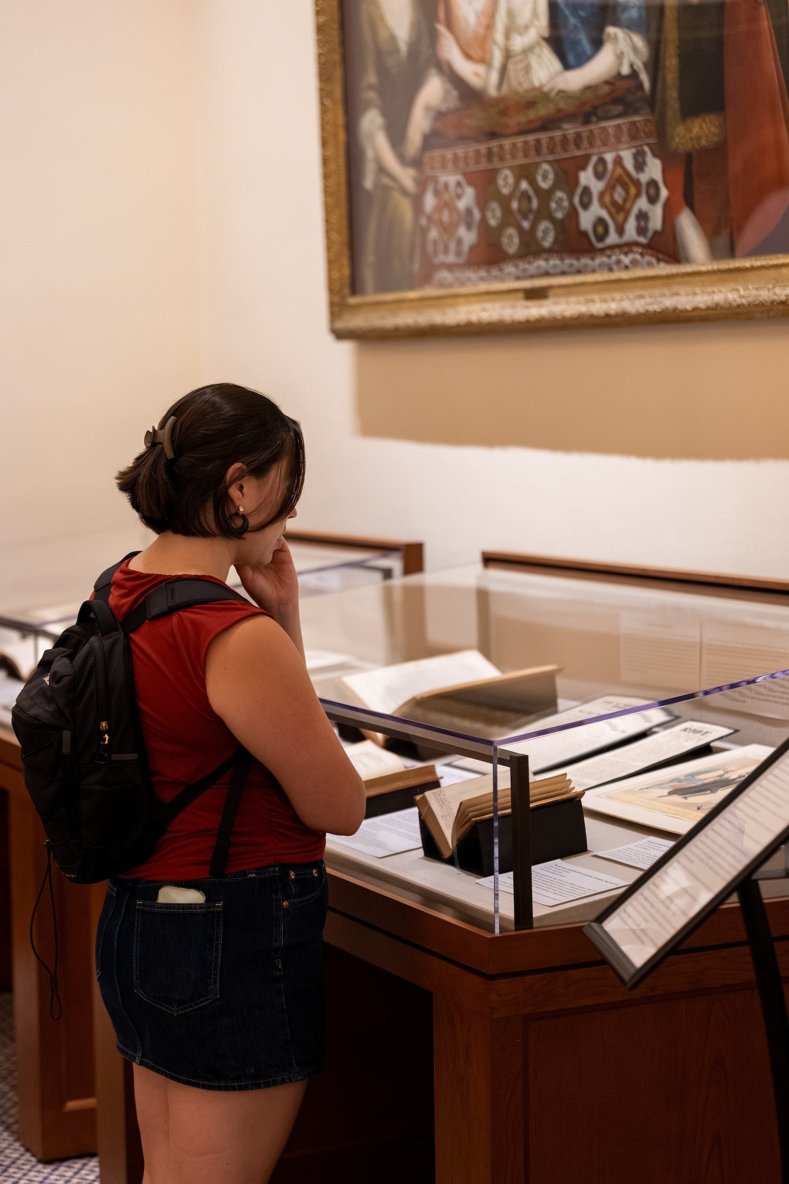 A student looks at a library exhibition of books behind a glass case.
