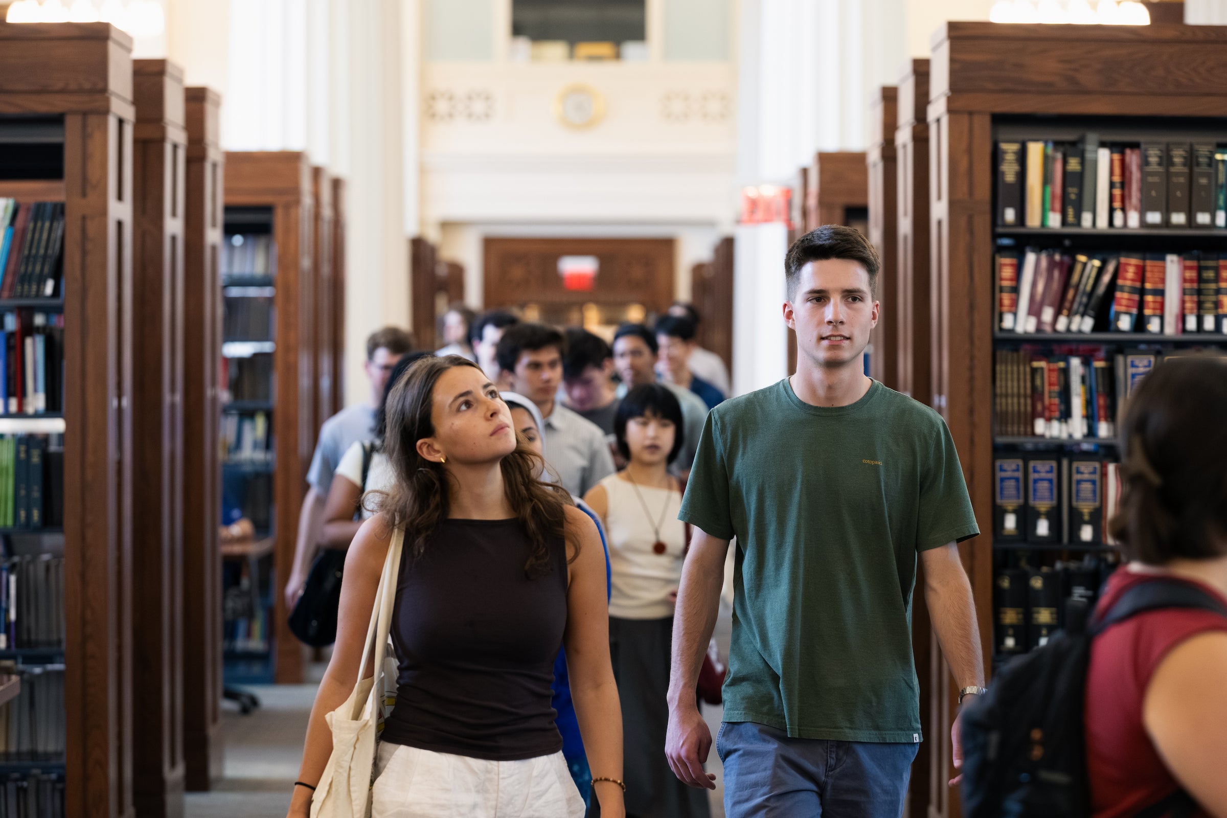 Students walk through a library and look around at their surroundings while on a tour.