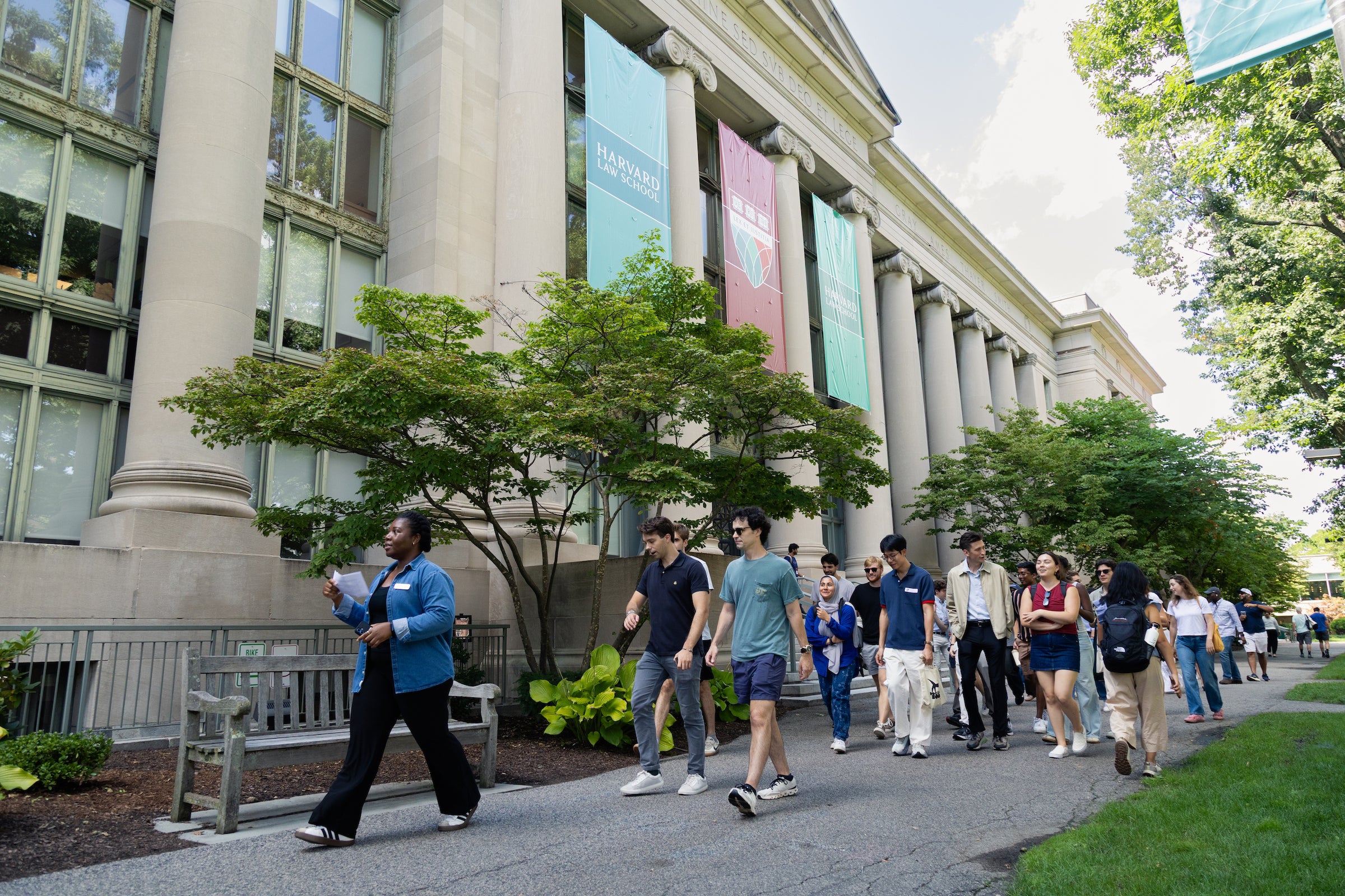 Students walk in front of Langdell Hall while following an individual giving a tour.