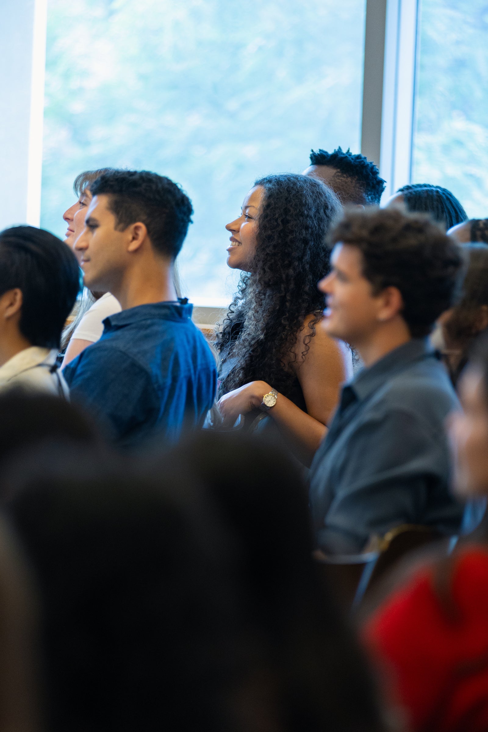 A student smiles while listening to a speaker while sitting in an audience.