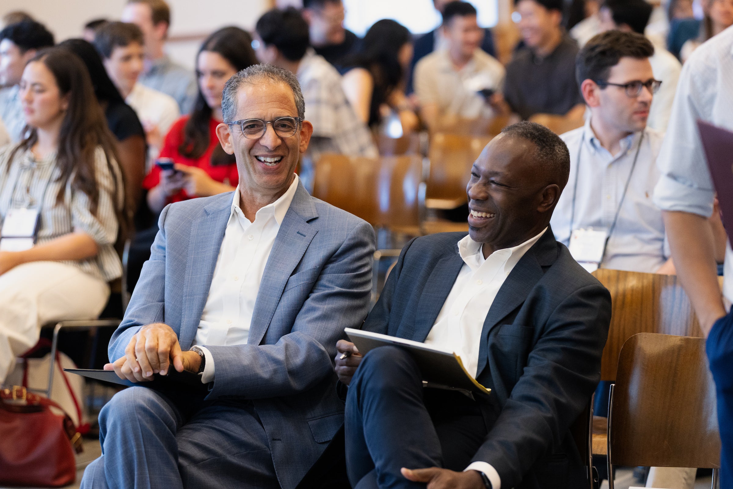 Dean Goldberg and Professor Charles laugh together while seated in an audience.
