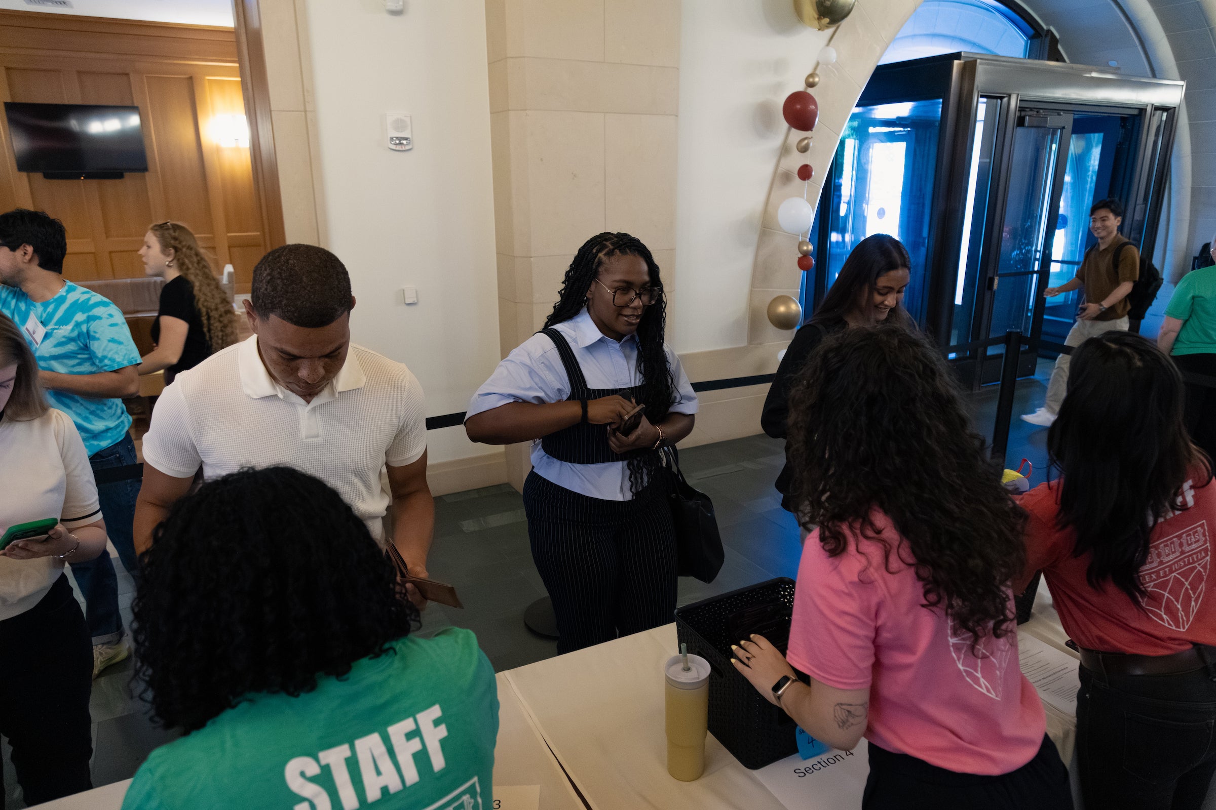 A group of students check in at a table in the entryway of a building.