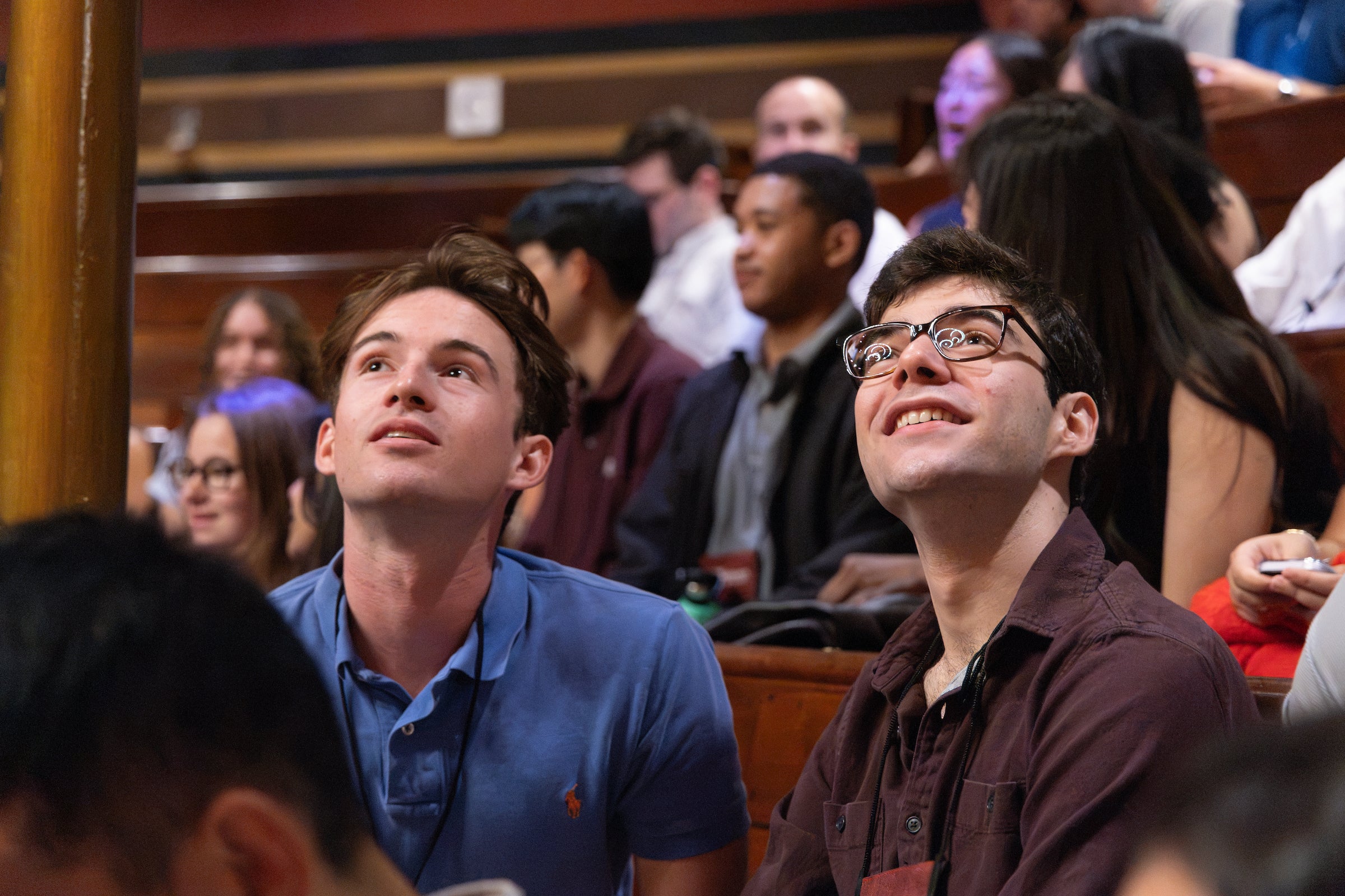 Two students in an auditorium look upward at their surroundings in a historic theater surrounded by other students.