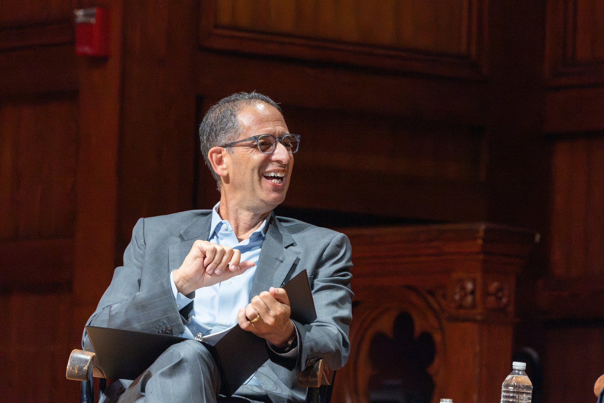 Dean Goldberg laughs while engaging in a discussion on the stage of a theatre.