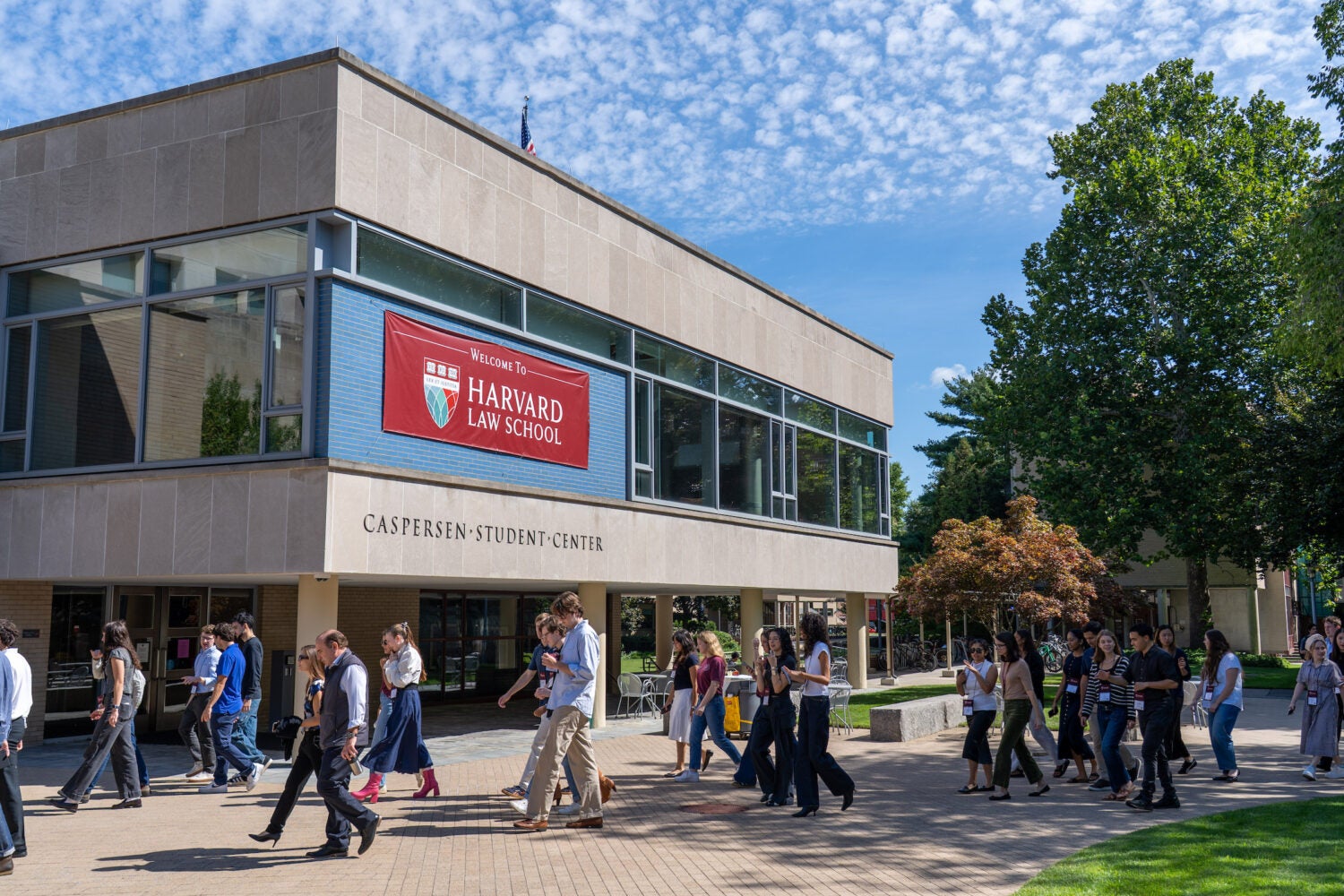 Students walk across a paved courtyard in front of the Harvard Law School Caspersen Student Center on a sunny day.