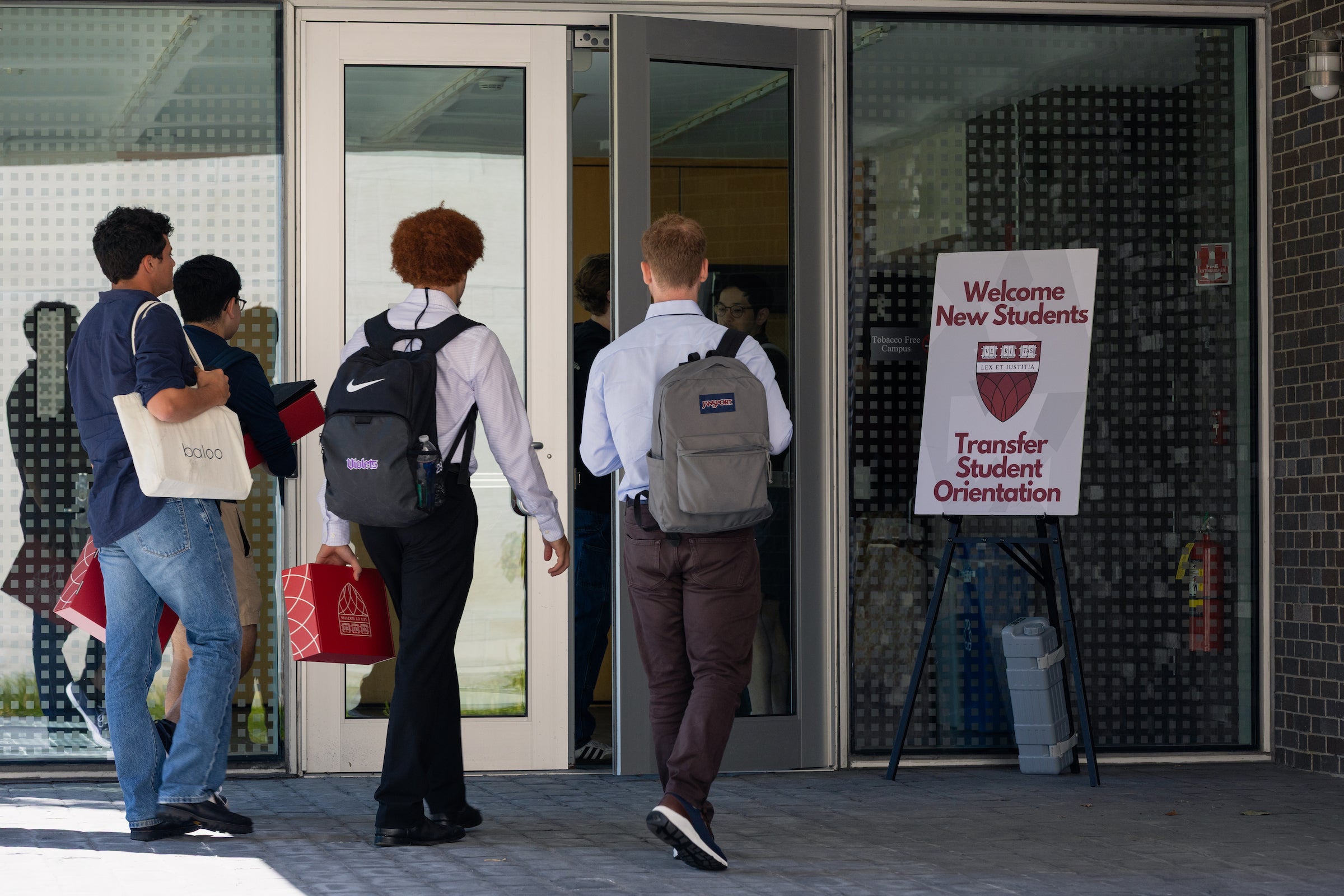 Students enter a building through glass doors, with a sign welcoming transfer students to orientation.