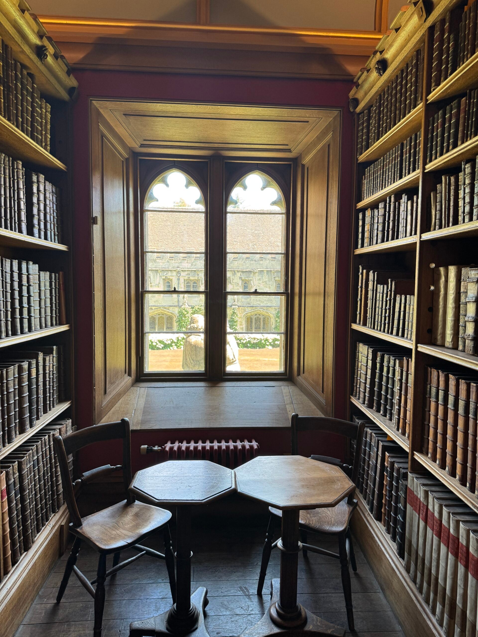 Narrow room with bookcases on both sides, a window in rear, and two small tables and chairs in forefront.